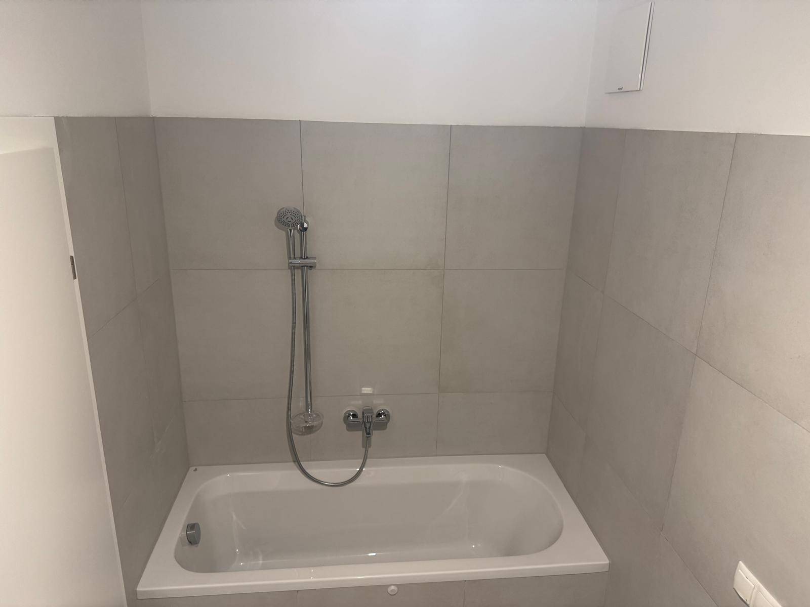 Modernes Badezimmer mit integrierter Badewanne und hellen Fliesen an den Wänden.