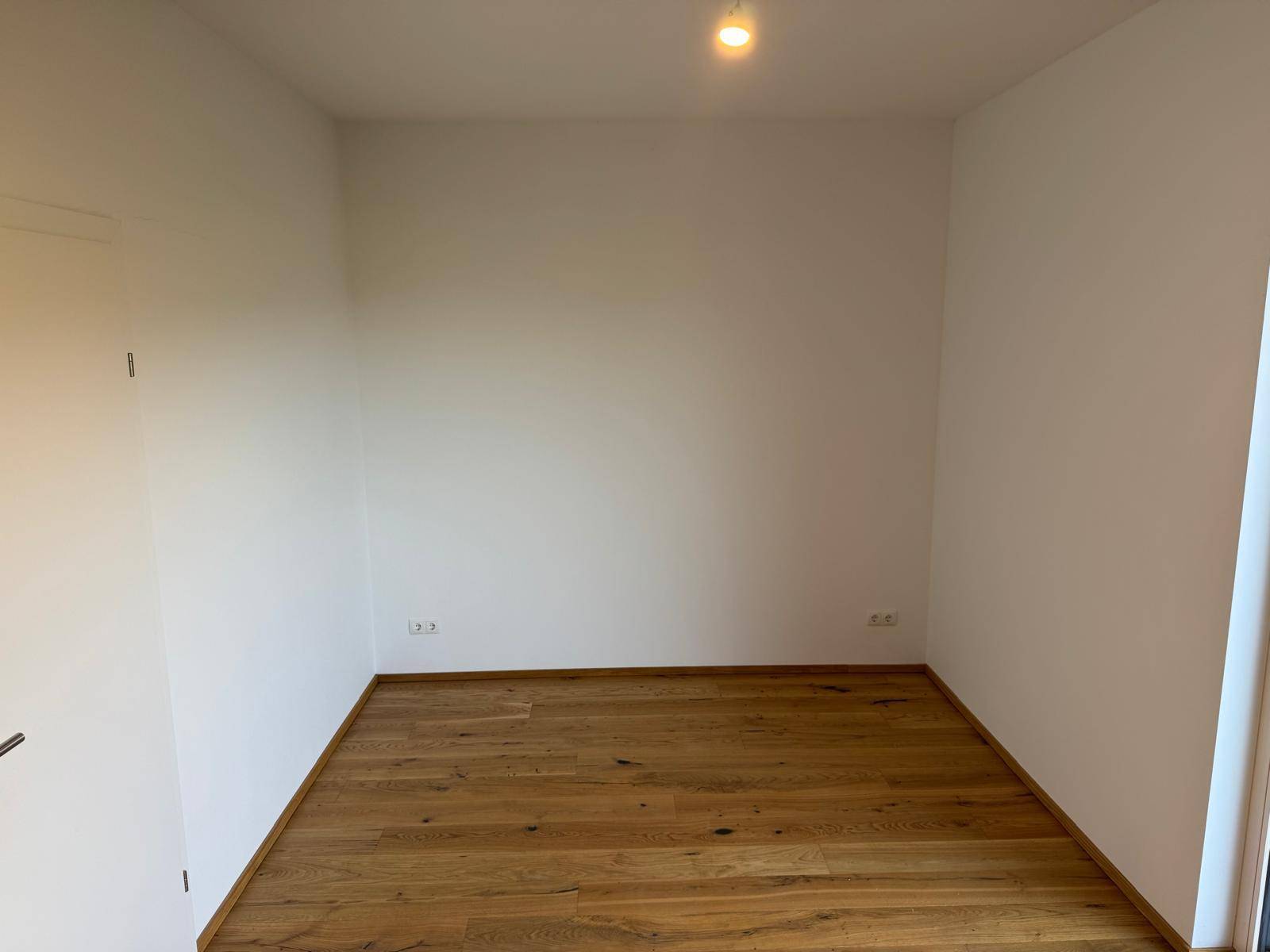 Leeres Zimmer mit hellem Holzboden und weißen Wänden, bereit für die individuelle Gestaltung.