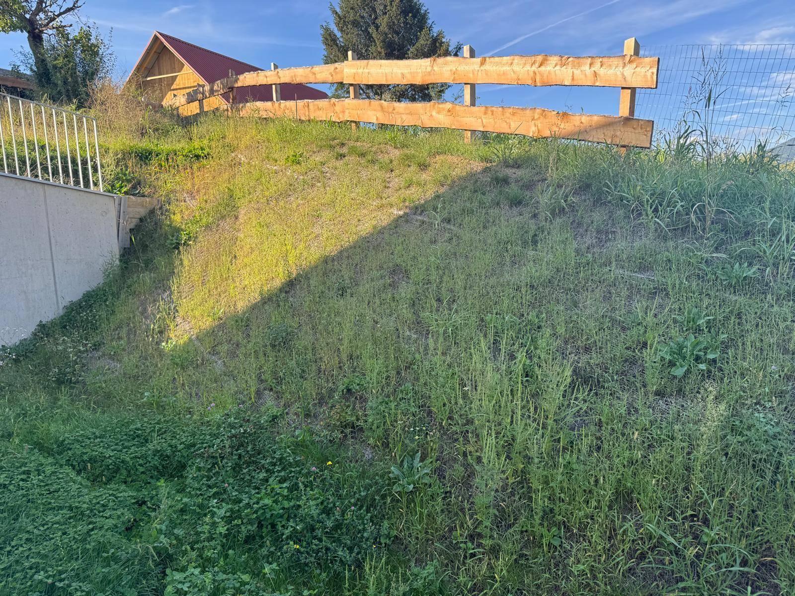 Grüner Hang mit rustikalem Holzzaun und Blick auf die umliegende Landschaft.