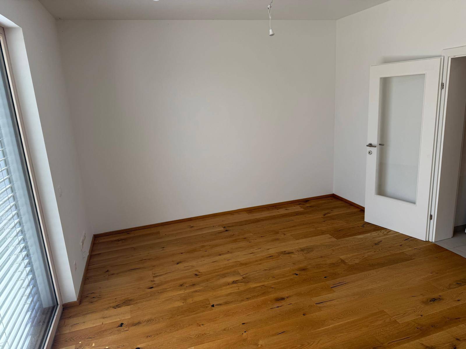 Lichtdurchfluteter Raum mit Holzboden, großen Fenstern und Jalousien, ideal für individuelle Gestaltung.