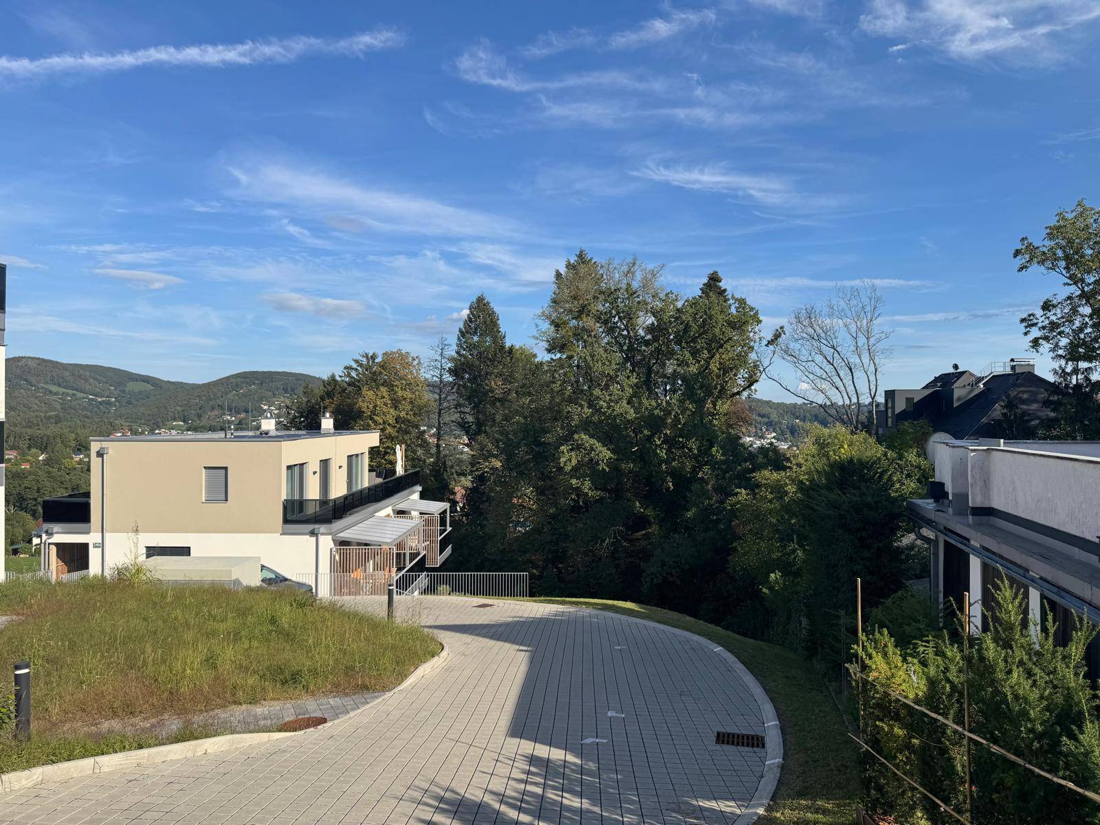 Moderne Wohngebäude in einer grünen Umgebung mit Hügeln im Hintergrund unter blauem Himmel.