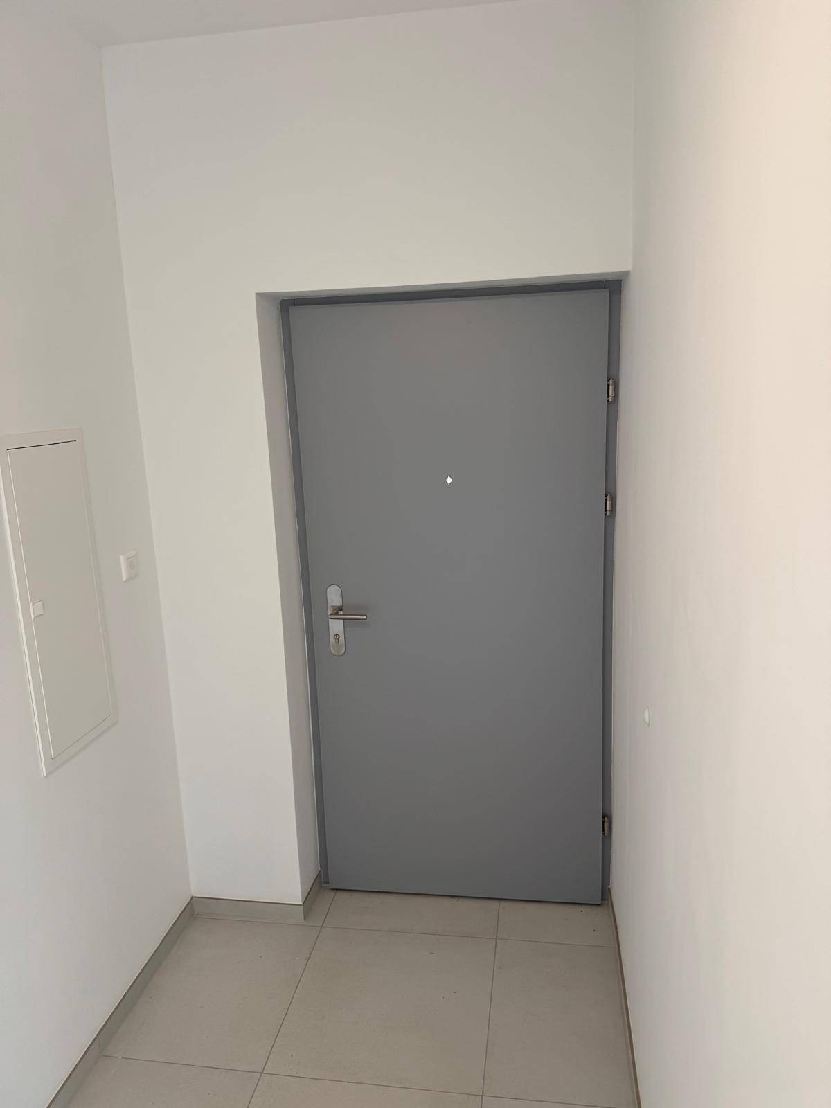 Eingangsbereich mit grauer Wohnungstür und hellen Fliesen, schlicht und funktional gestaltet.