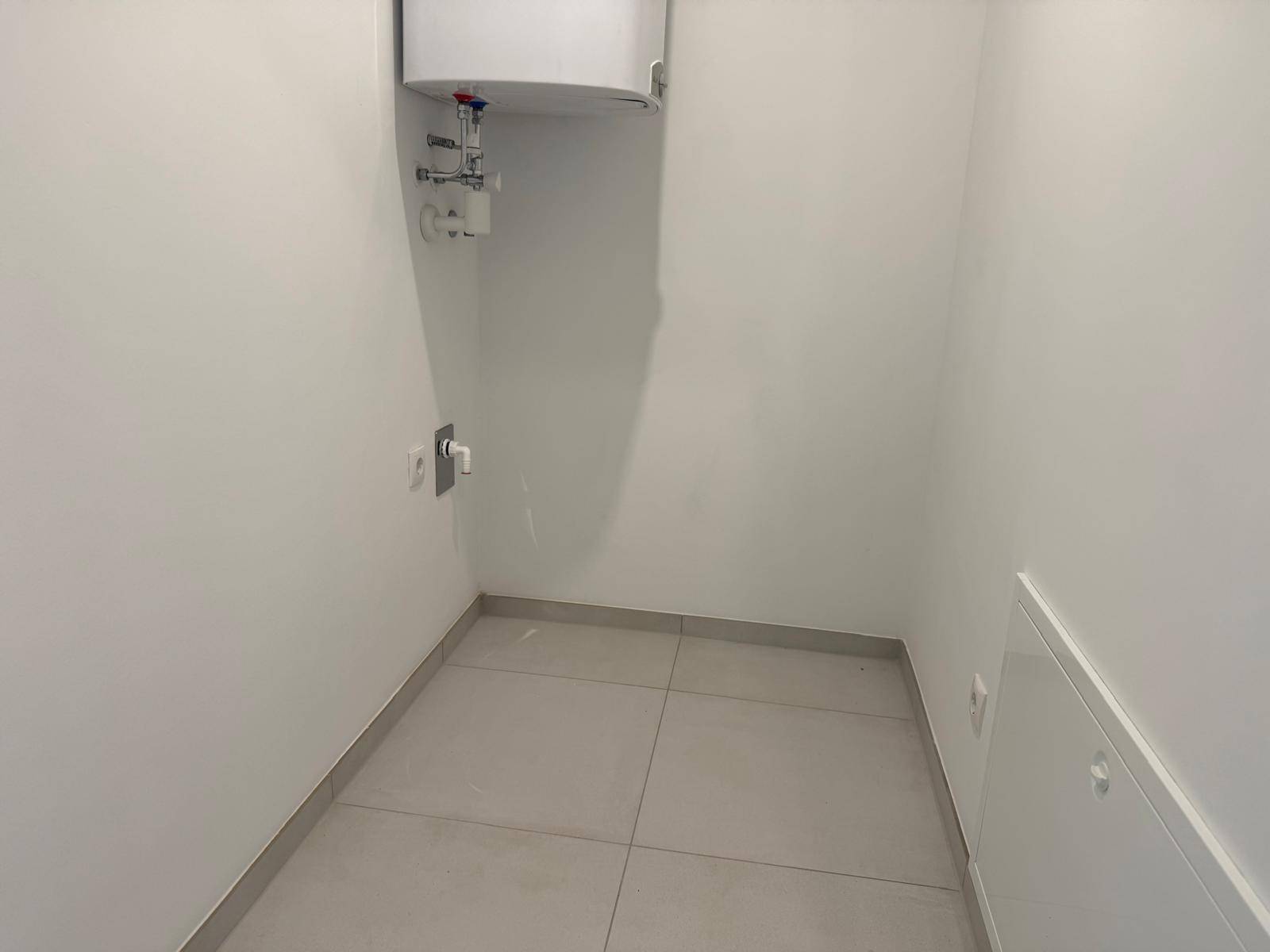 Kleiner Hauswirtschaftsraum mit Fliesenboden und Warmwasserboiler an der Wand.