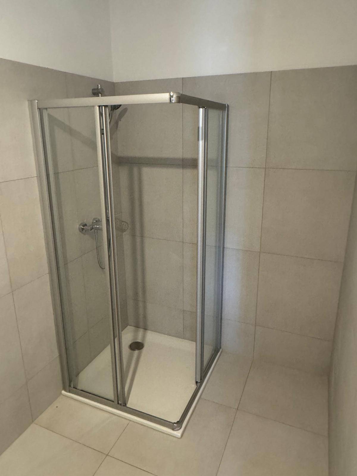 Modernes Badezimmer mit Duschkabine und hellen Fliesen an Wänden und Boden.