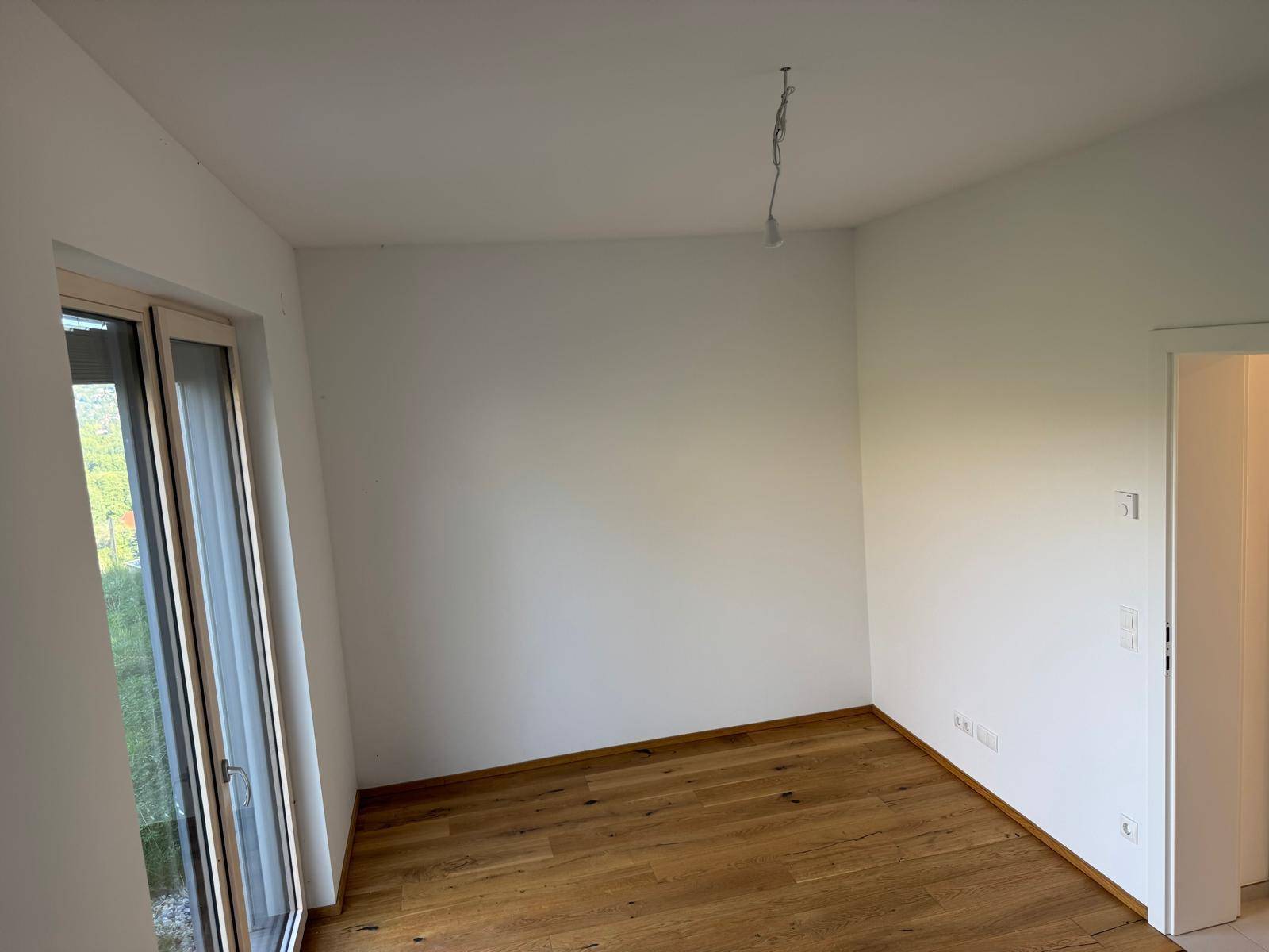 Leeres Zimmer mit hellem Holzboden und weiß gestrichenen Wänden, bereit zur Einrichtung.