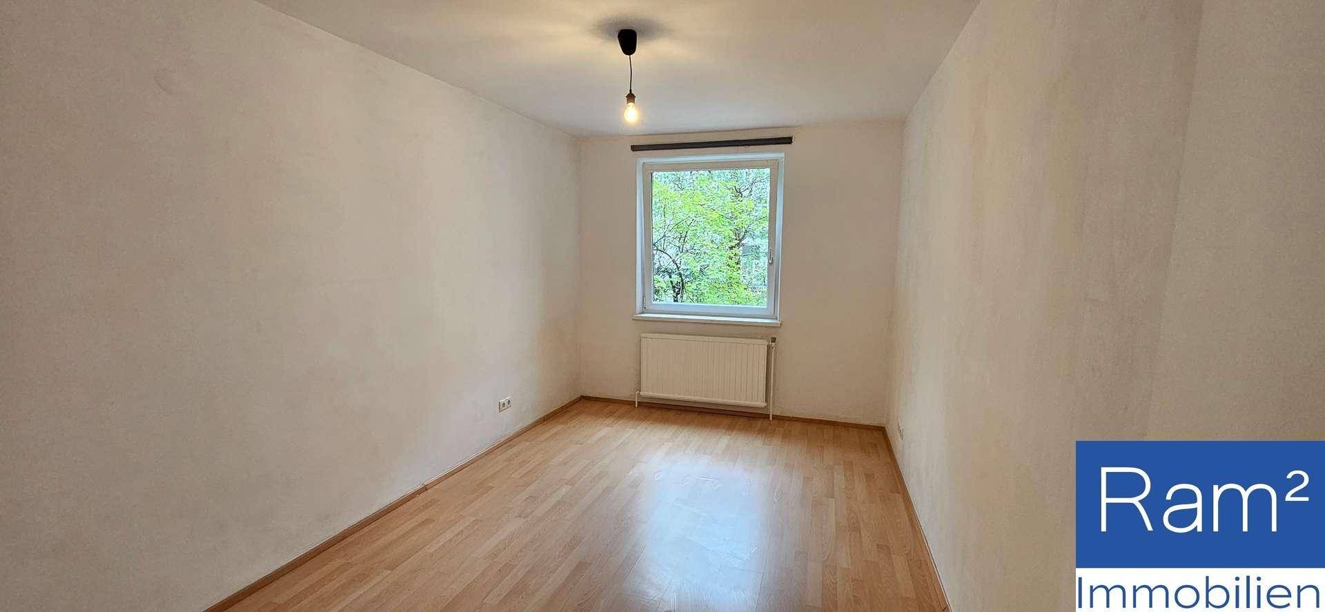 Geräumiges Zimmer mit Holzboden und einem großen Fenster mit Blick ins Grüne.