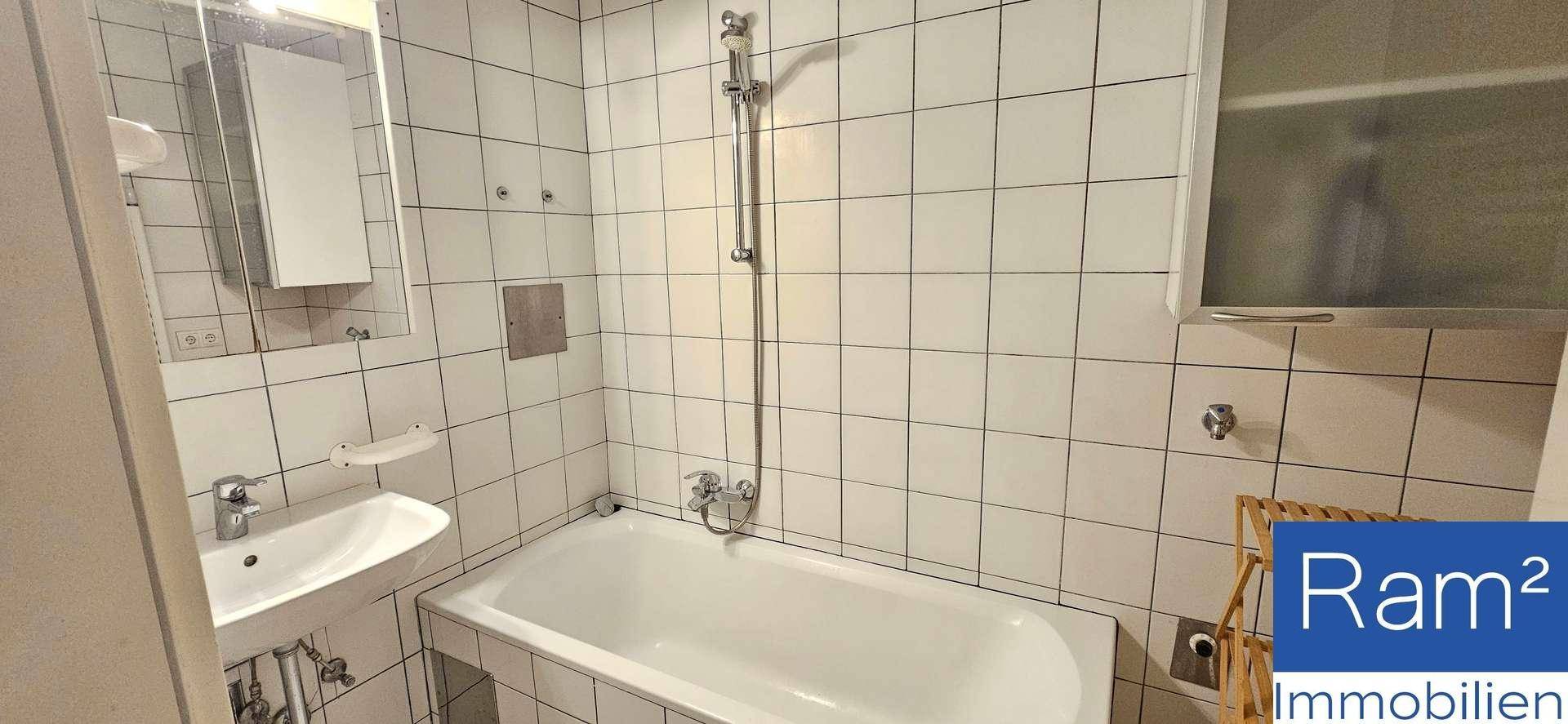 Gefliestes Badezimmer mit Badewanne, Duscharmatur und einem kleinen Waschbecken.