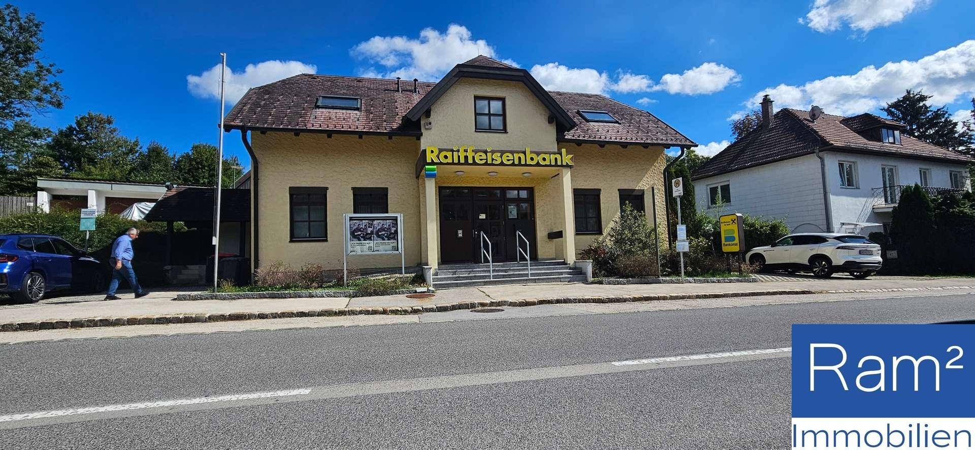 Gebäude der Raiffeisenbank an einer Straße mit parkenden Autos und weiteren Häusern.