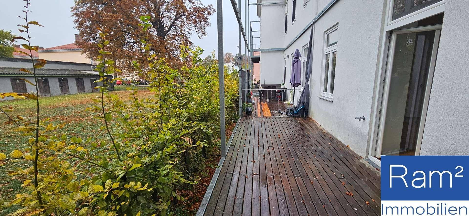 Langer Balkon mit Holzbelag entlang der Hausfassade und Blick auf den Garten.