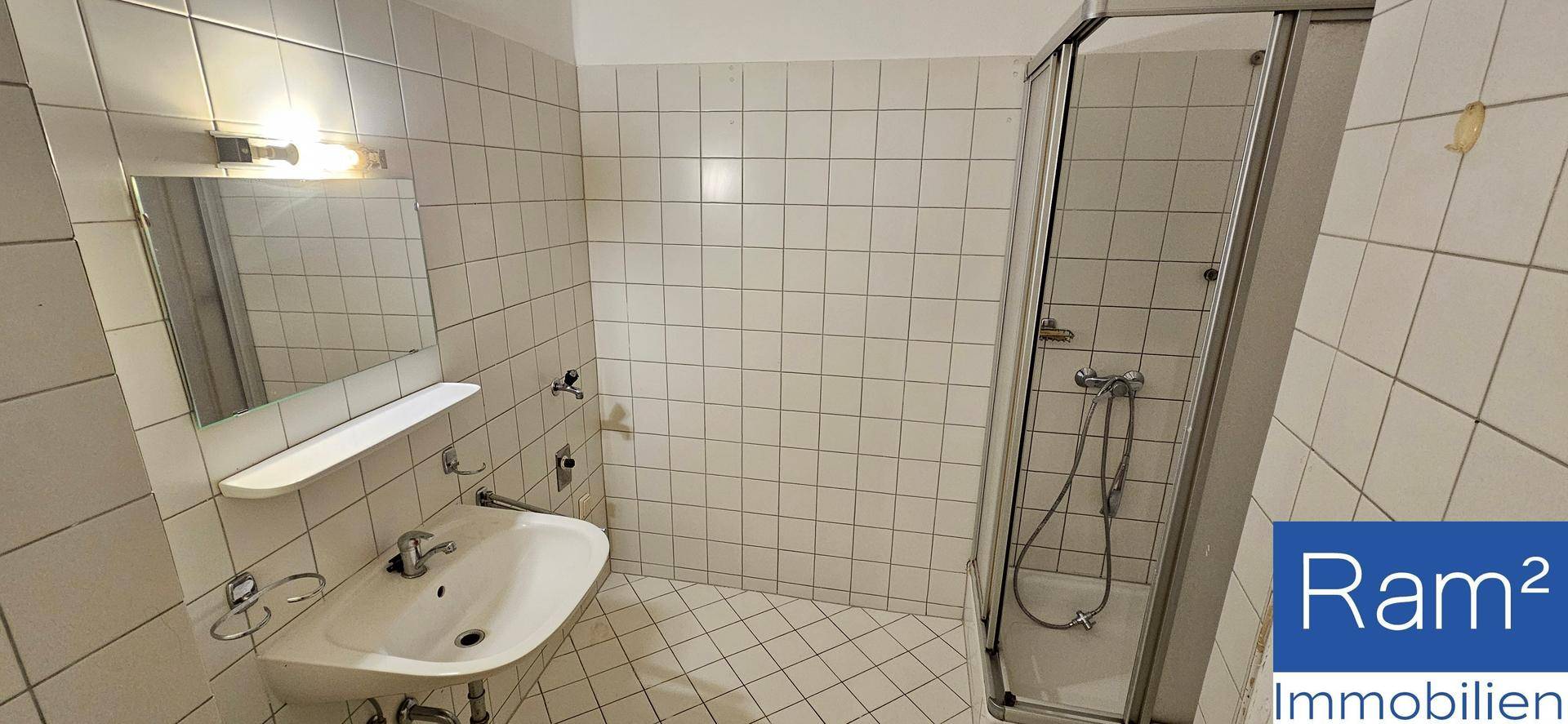 Gefliestes Badezimmer mit Duschkabine, Waschbecken und Spiegel, in gutem Zustand.
