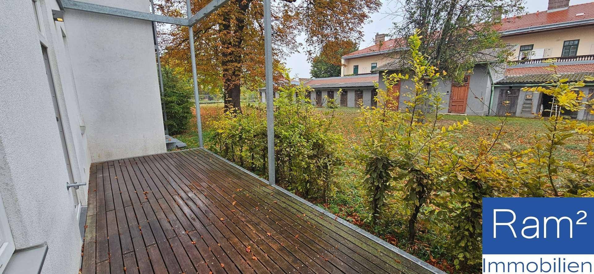Balkon mit Holzbelag und Blick ins Grüne sowie auf umliegende Gebäude.