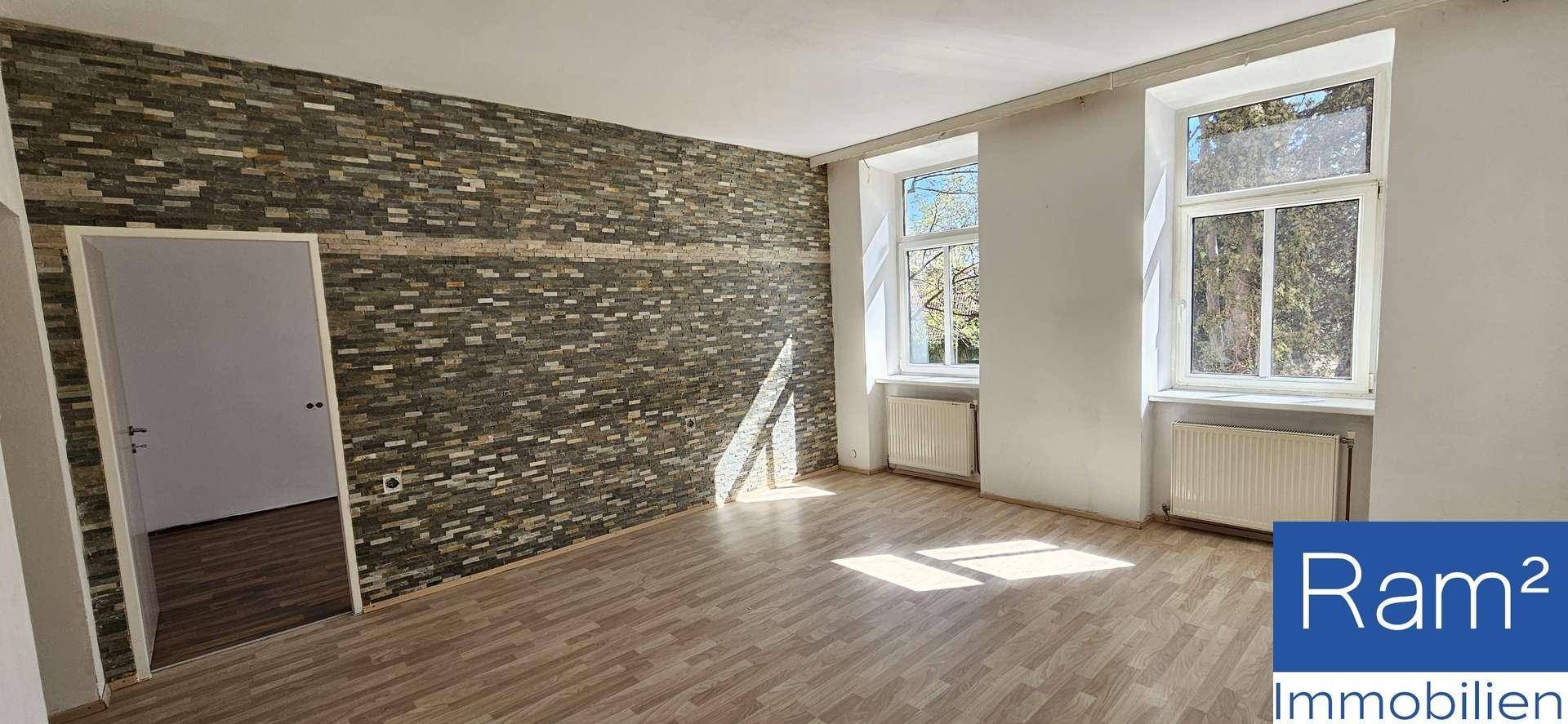 Geräumiger Wohnbereich mit dekorativer Steinwand, Laminatboden und Zugang zu einem weiteren Zimmer.