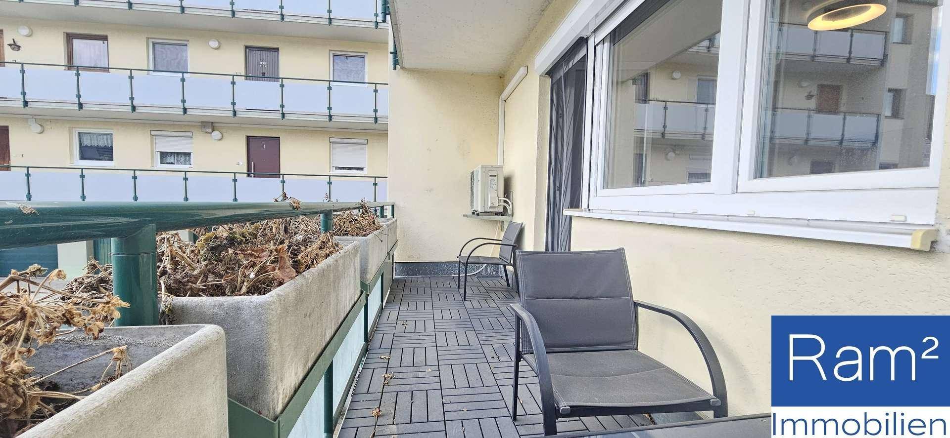 Möblierter Balkon mit dunklem Fliesenboden und Blick auf gegenüberliegende Wohngebäude.