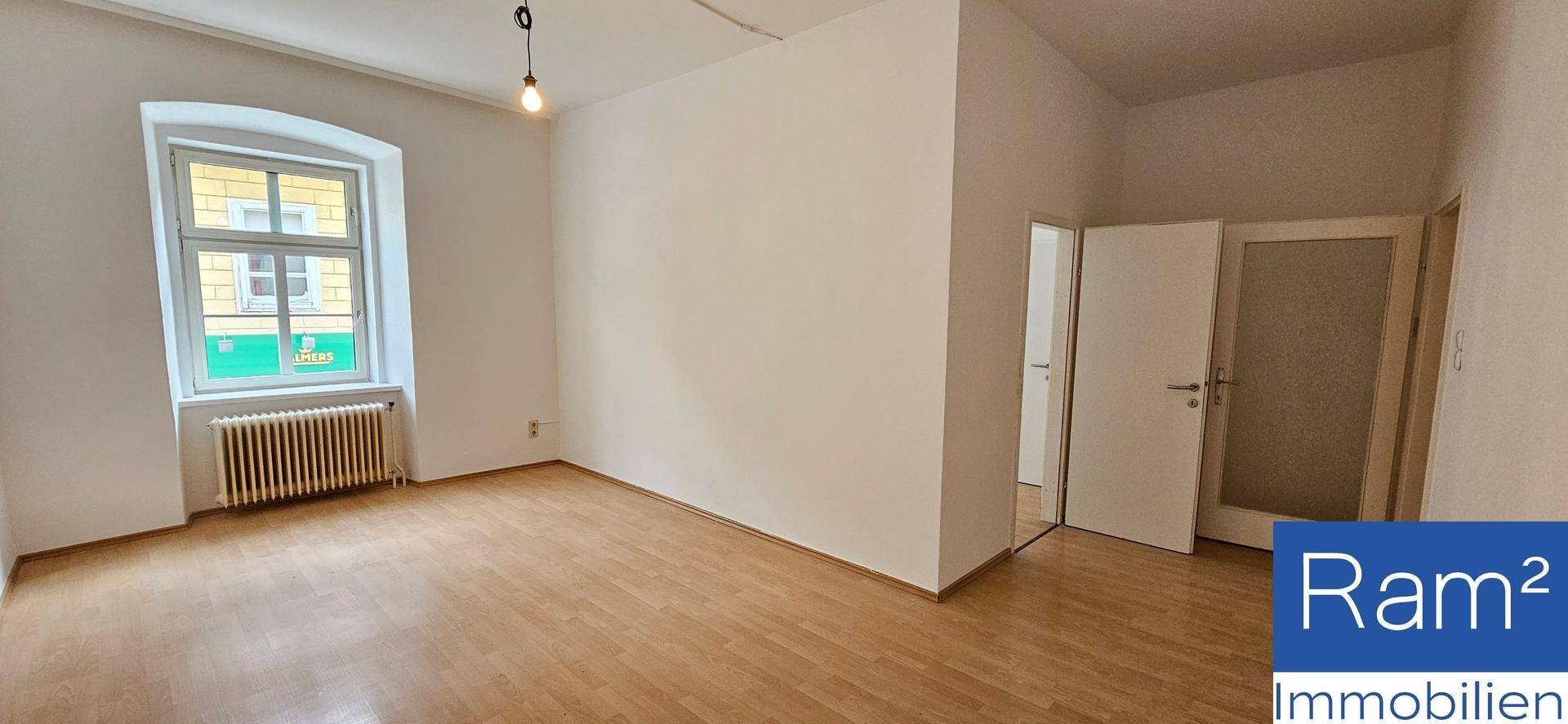Leerer Raum mit Laminatboden, einem Fenster und Heizkörper, bereit zur individuellen Gestaltung.