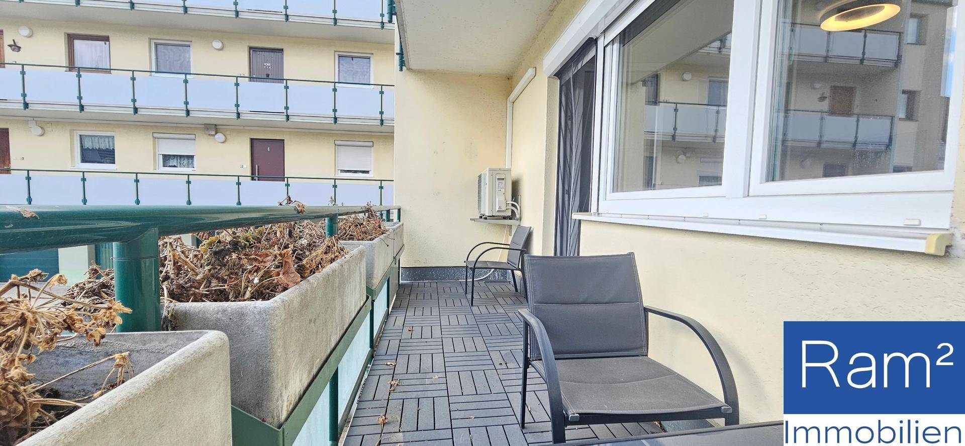 Ein gepflegter Balkon mit grauen Bodenfliesen, Sitzgelegenheiten und Blick auf die umliegenden Gebäude.
