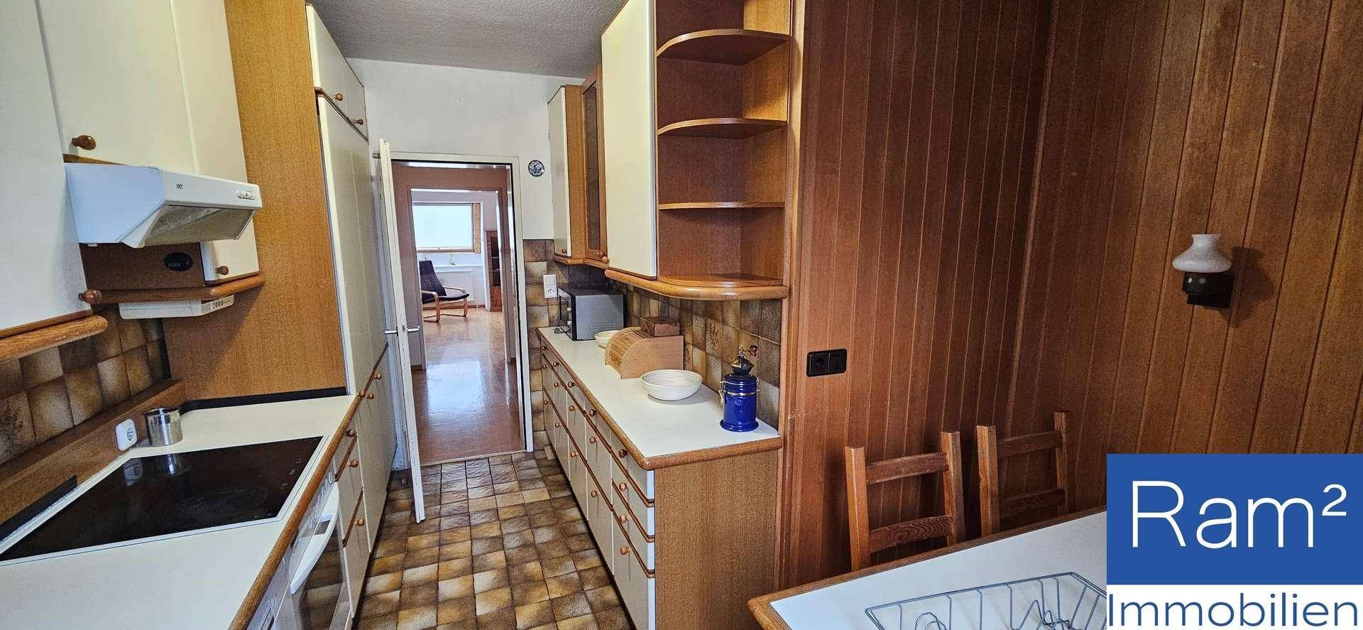 Funktionale Küche mit weißen Schränken, Holzvertäfelung und grundlegenden Geräten.