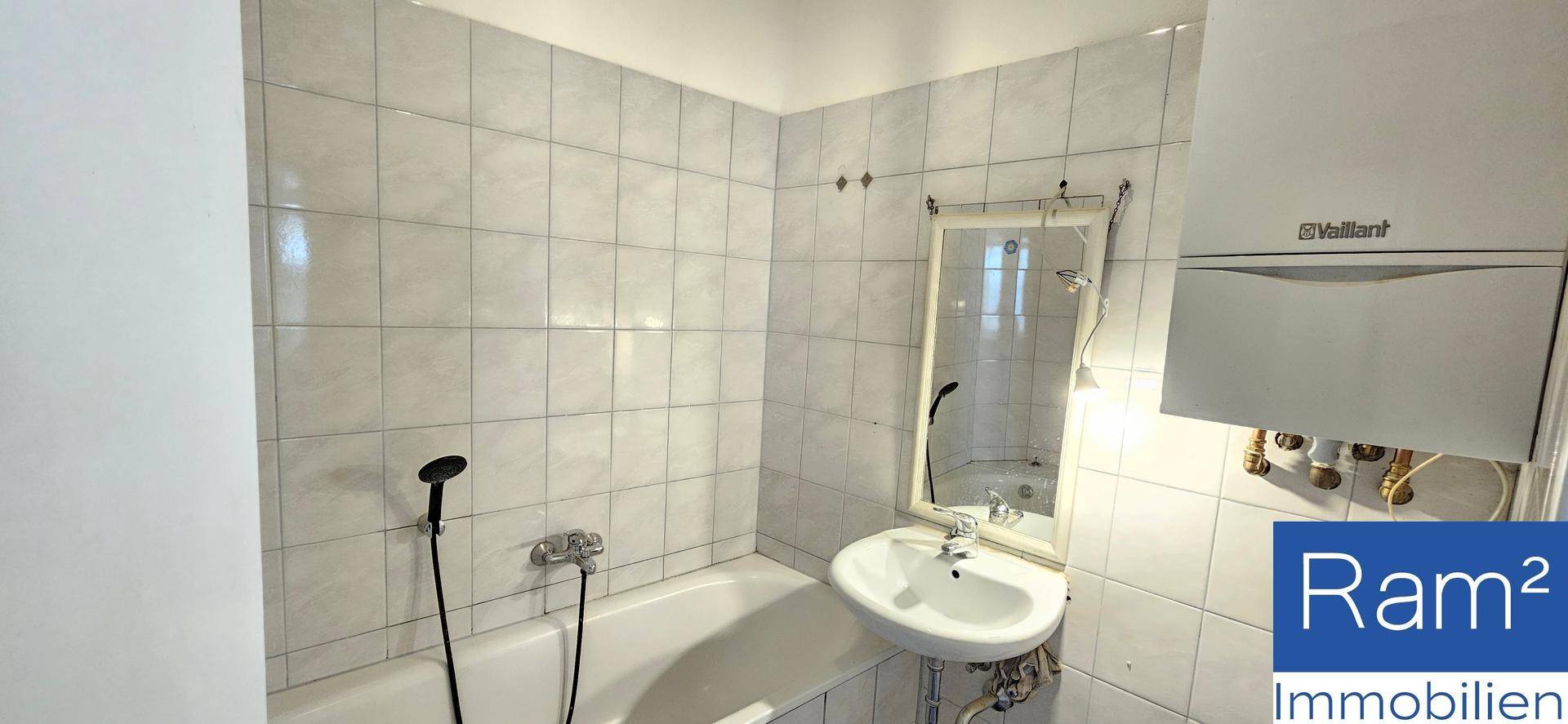 Gefliestes Badezimmer mit Badewanne, Waschbecken und Warmwasserboiler an der Wand.