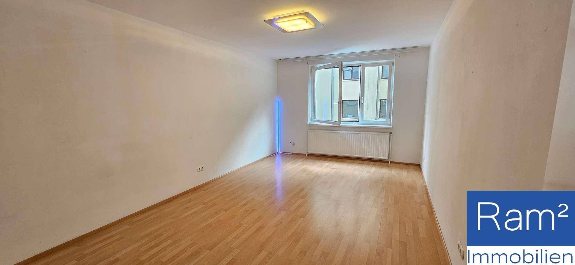 Heller Wohnraum mit Holzboden und einem großen Fenster, das den Raum mit Licht füllt.