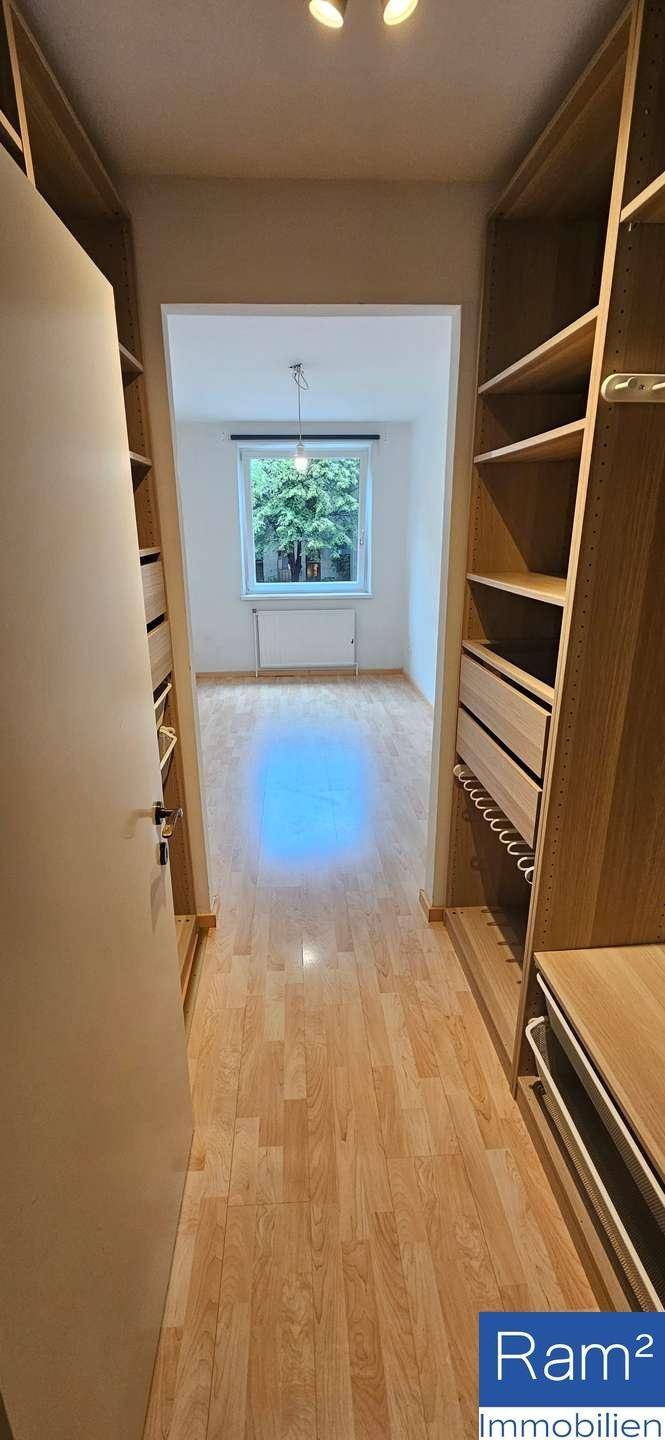 Langer Flur mit eingebauten Holzregalen und Blick in ein helles Zimmer mit Fenster.