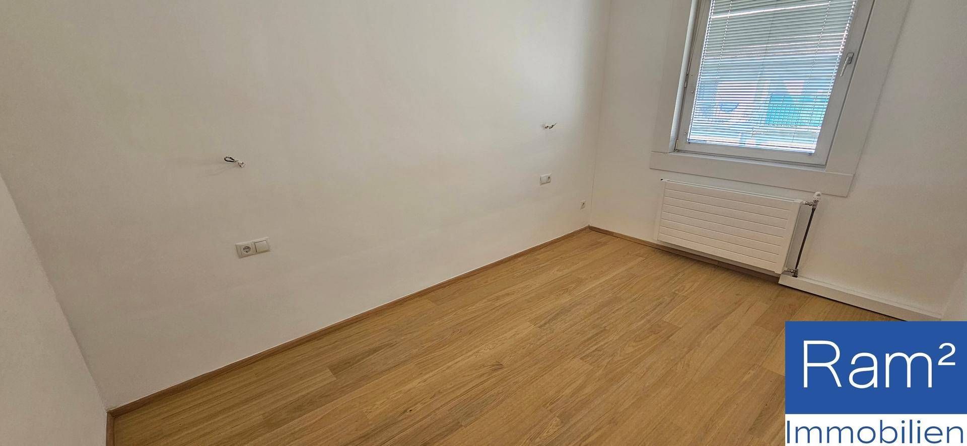 Schlichtes Schlafzimmer mit Laminatboden und einem Fenster, das für natürliche Belüftung sorgt.