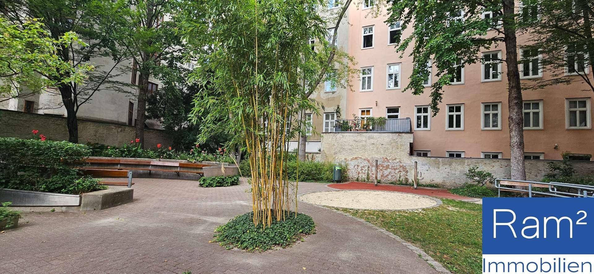 Ruhiger Innenhof mit Sitzgelegenheiten, Bäumen und einem Sandbereich, ideal zum Entspannen.