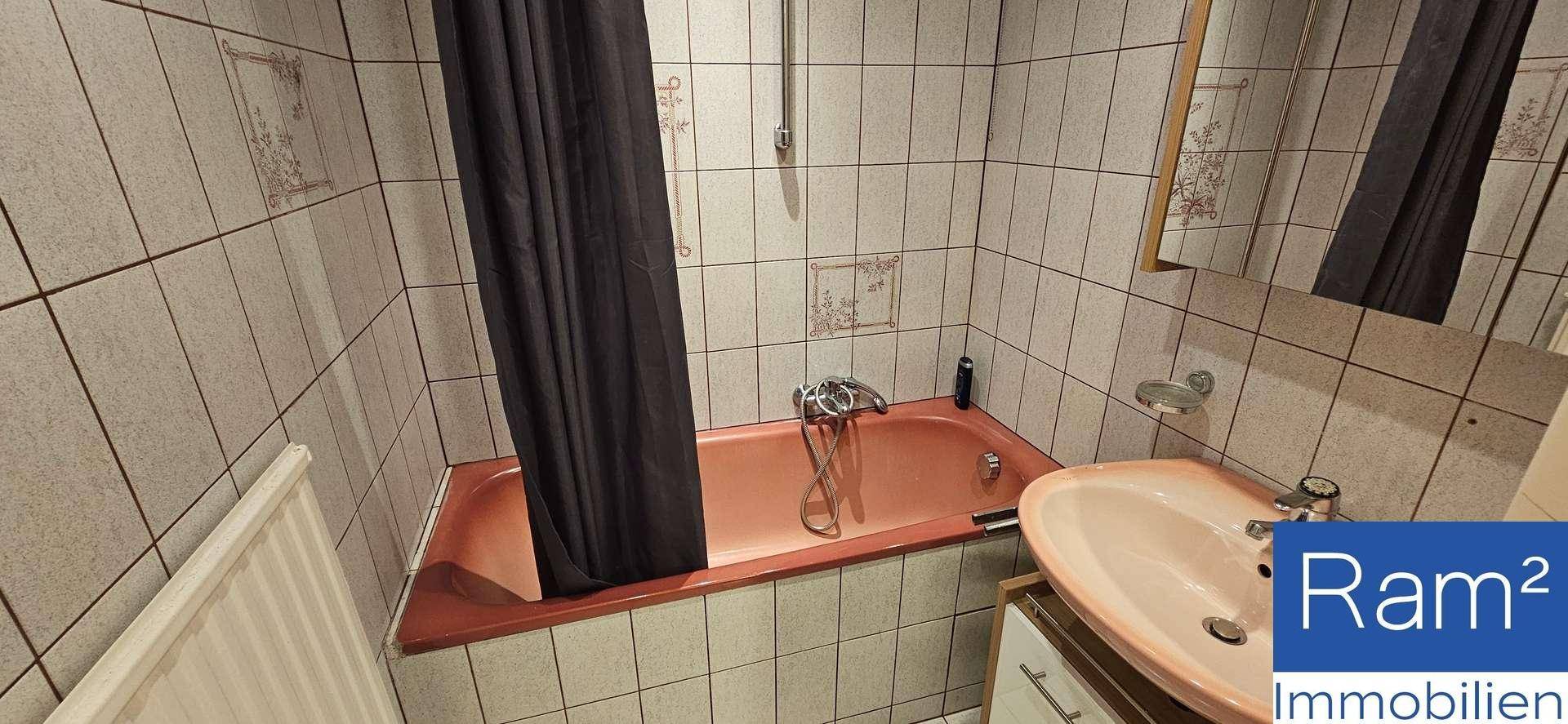 Badezimmer mit Badewanne, Waschbecken und hellen Fliesen im 80er-Jahre-Stil.