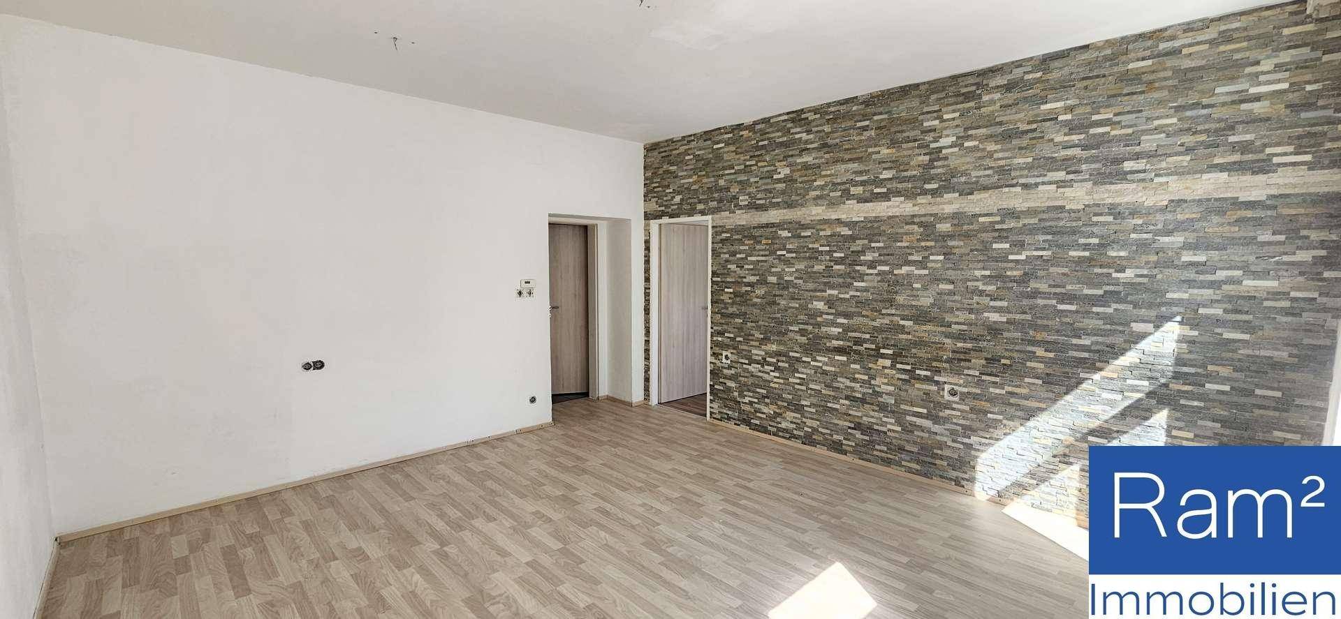 Lichtdurchfluteter Wohnraum mit moderner Steinwand und hellem Laminatboden, bereit zur individuellen Gestaltung.