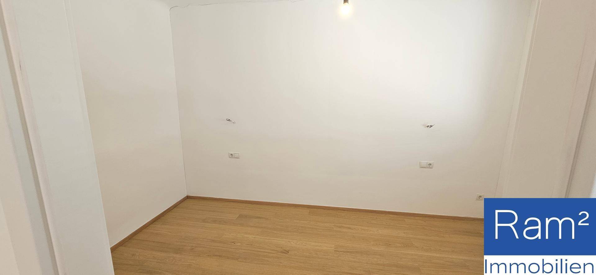 Leeres Zimmer mit Laminatboden und weißen Wänden, bereit zur individuellen Gestaltung.