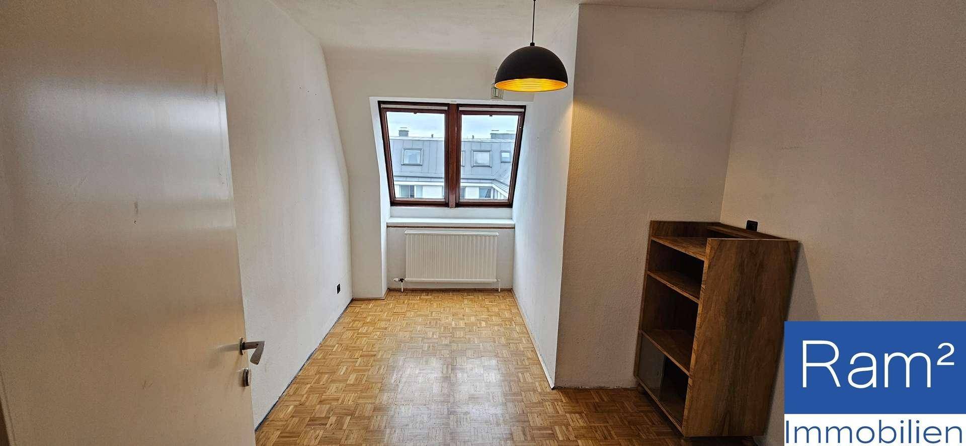 Helles Zimmer mit Parkettboden, Dachschrägenfenster und einem Bücherregal.