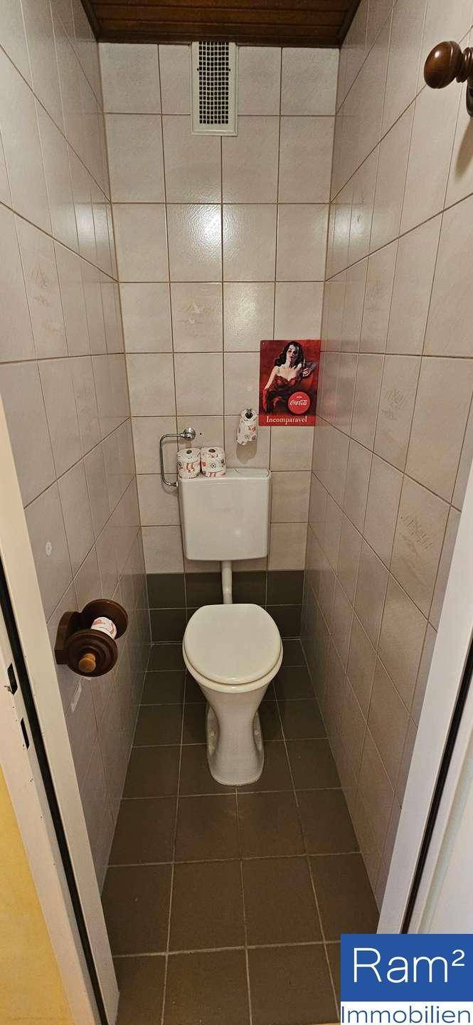 Separates WC mit Toilette und hellen Fliesen, funktional und einfach gehalten.