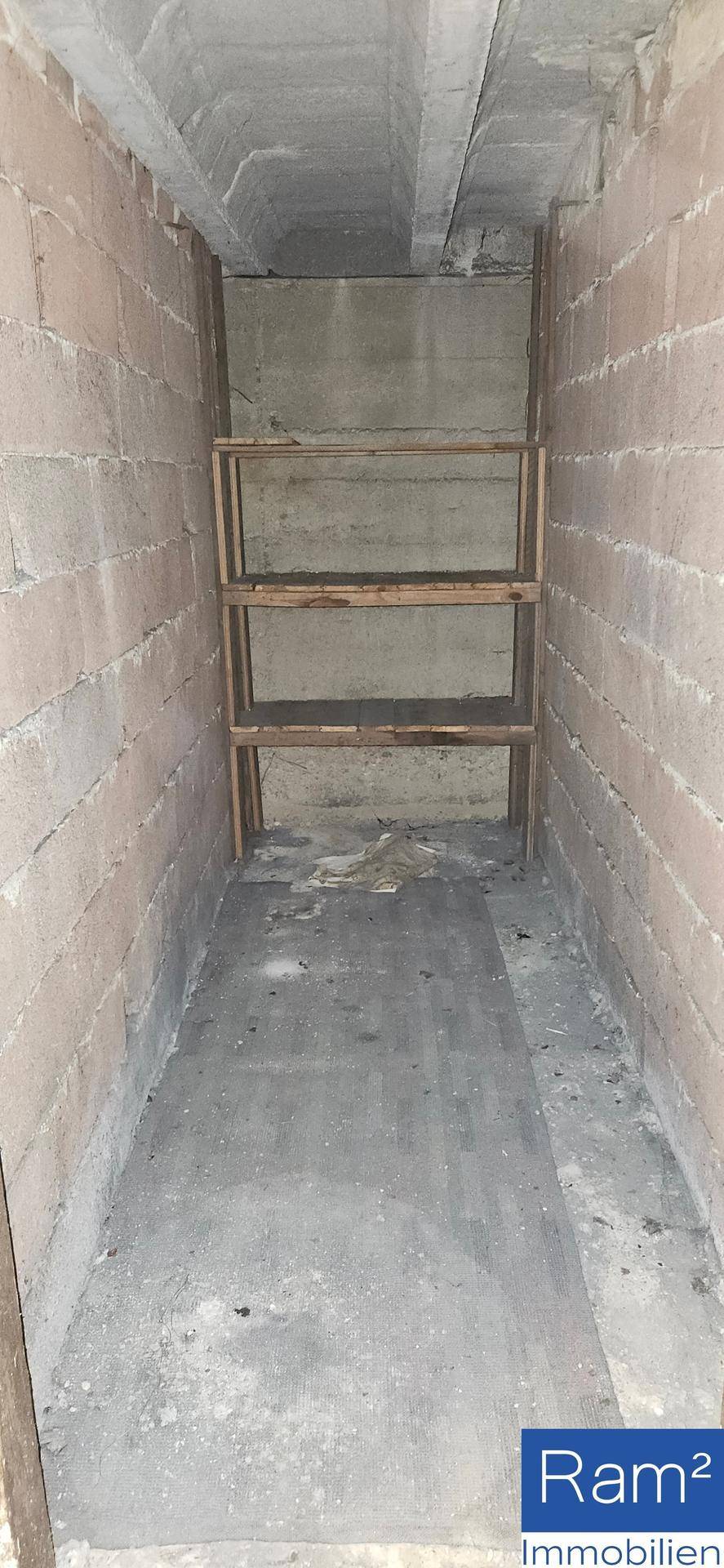 Praktischer Abstellraum mit Betonboden und einfachen Holzregalen für zusätzlichen Stauraum.