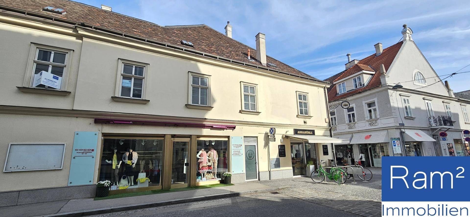 Historisches Gebäude mit Geschäften und Wohnungen an einer sonnigen Straße in einer charmanten Stadt.