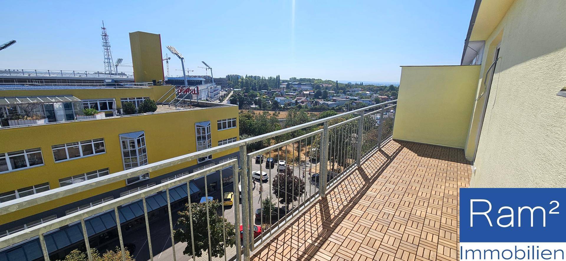 Geräumiger Balkon mit Holzbodenfliesen und Blick auf die umliegende Stadtlandschaft.