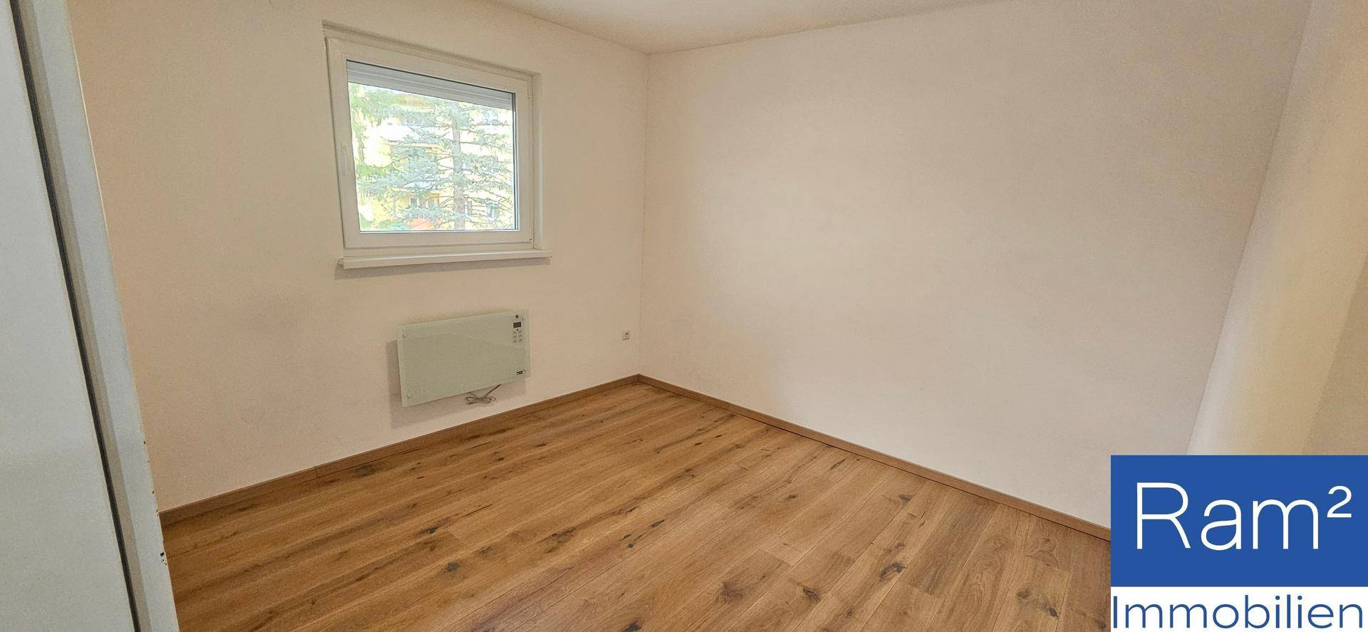 Helles Zimmer mit Holzfußboden, Fenster und Heizkörper.