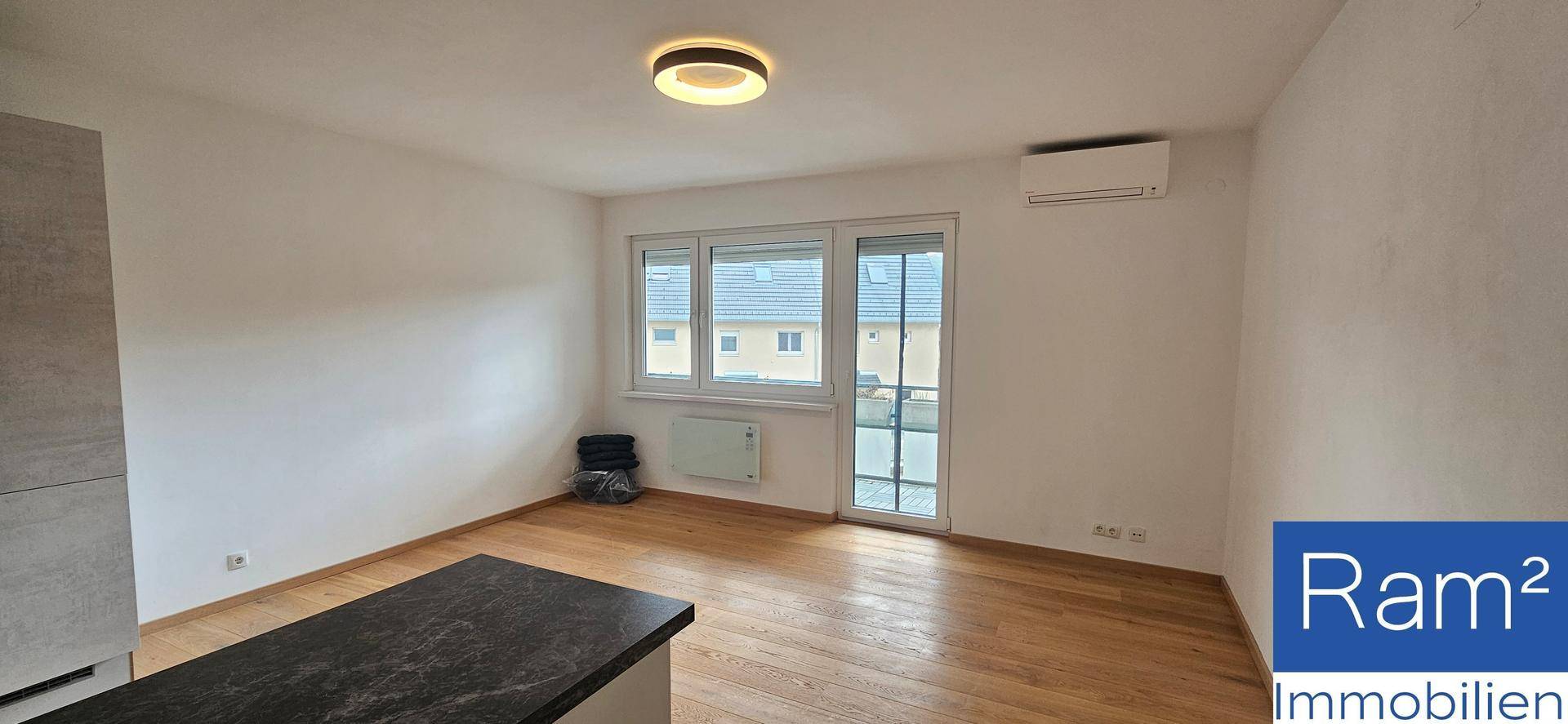 Heller Wohnraum mit Holzfußboden, großem Fenster und installierter Klimaanlage.