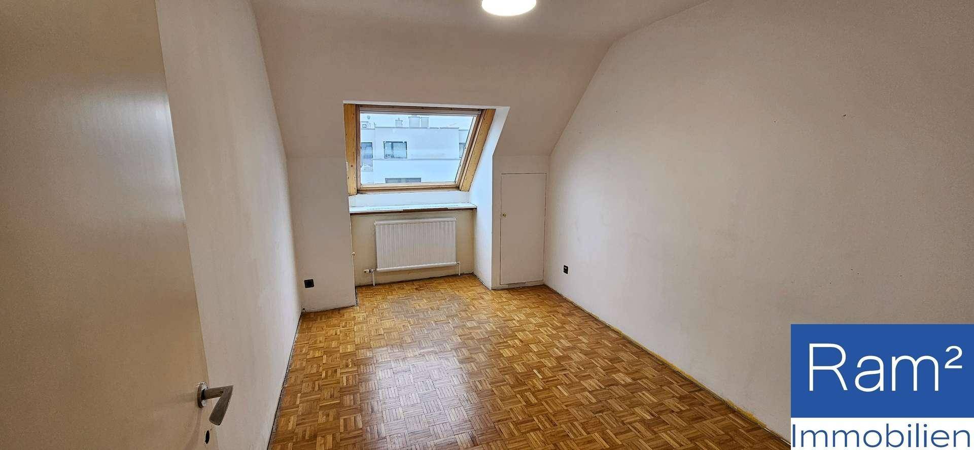 Geräumiges Zimmer mit Parkettboden und viel Tageslicht durch das Dachschrägenfenster.
