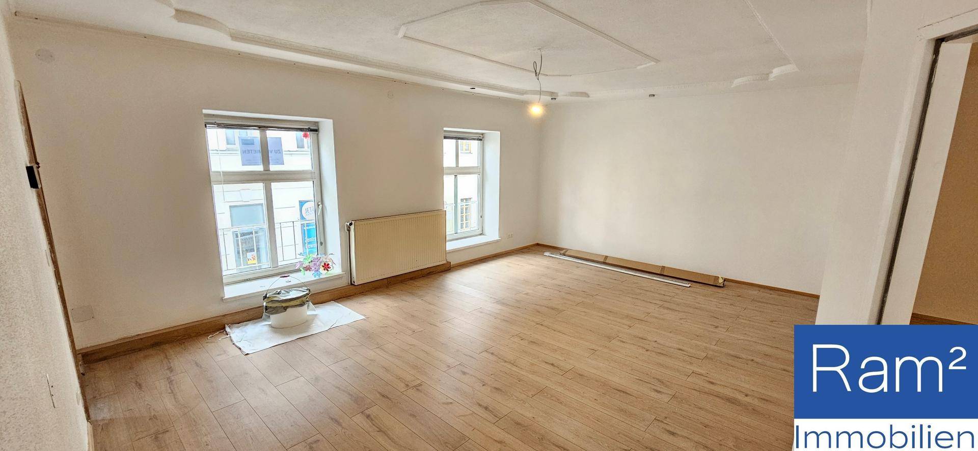 Heller, leerer Raum mit Holzboden und zwei Fenstern, ideal für Wohn- oder Schlafzimmer.