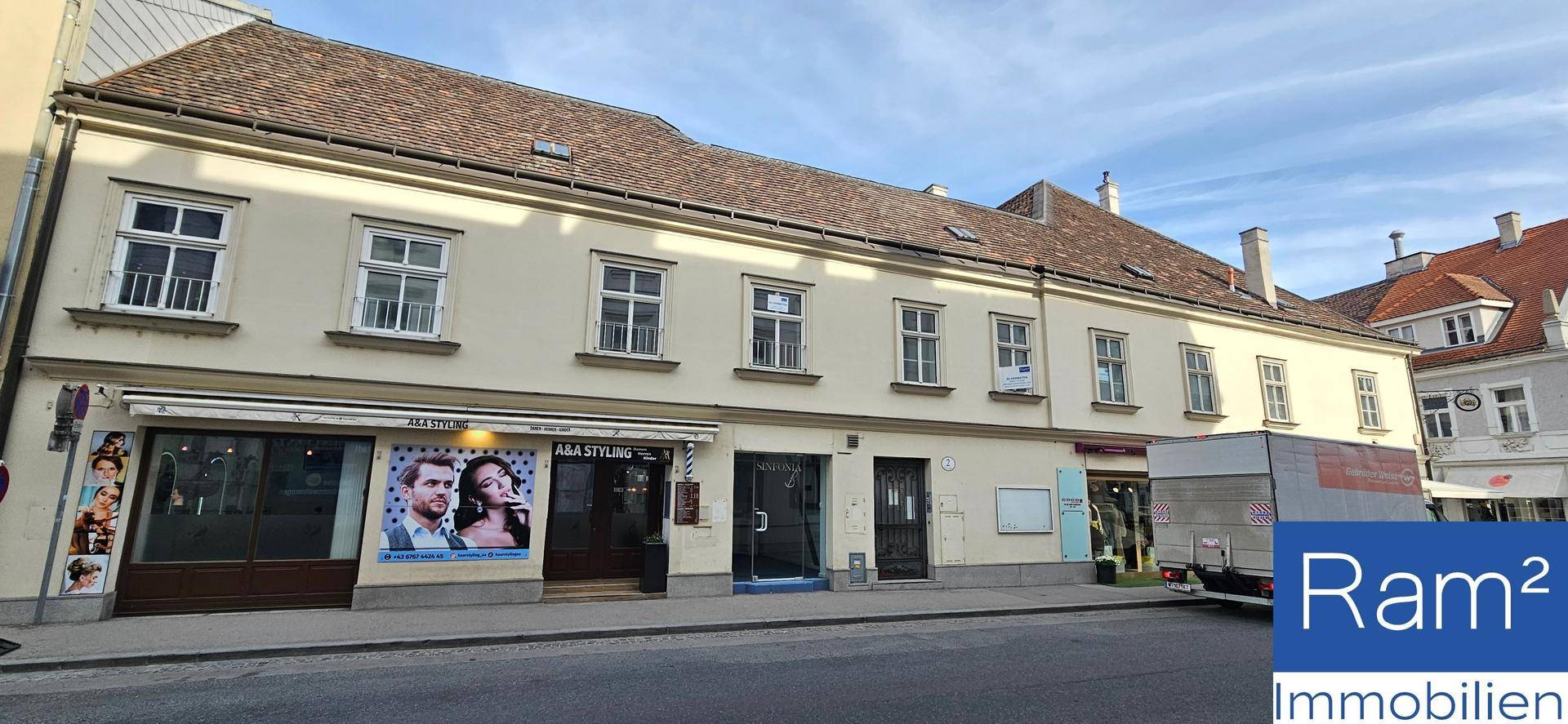 Fassade eines historischen Gebäudes mit mehreren Geschäften und Wohnungen in einer städtischen Umgebung.