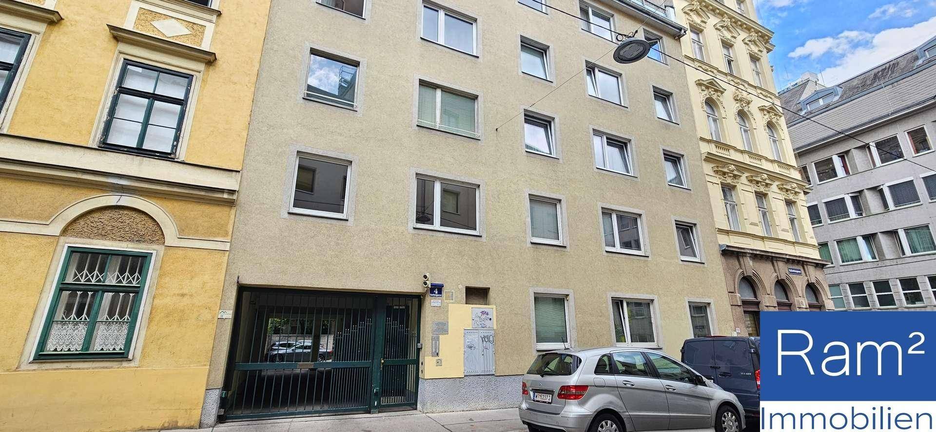 Wohngebäude mit mehreren Etagen und einer Garage im Erdgeschoss, umgeben von anderen Gebäuden.