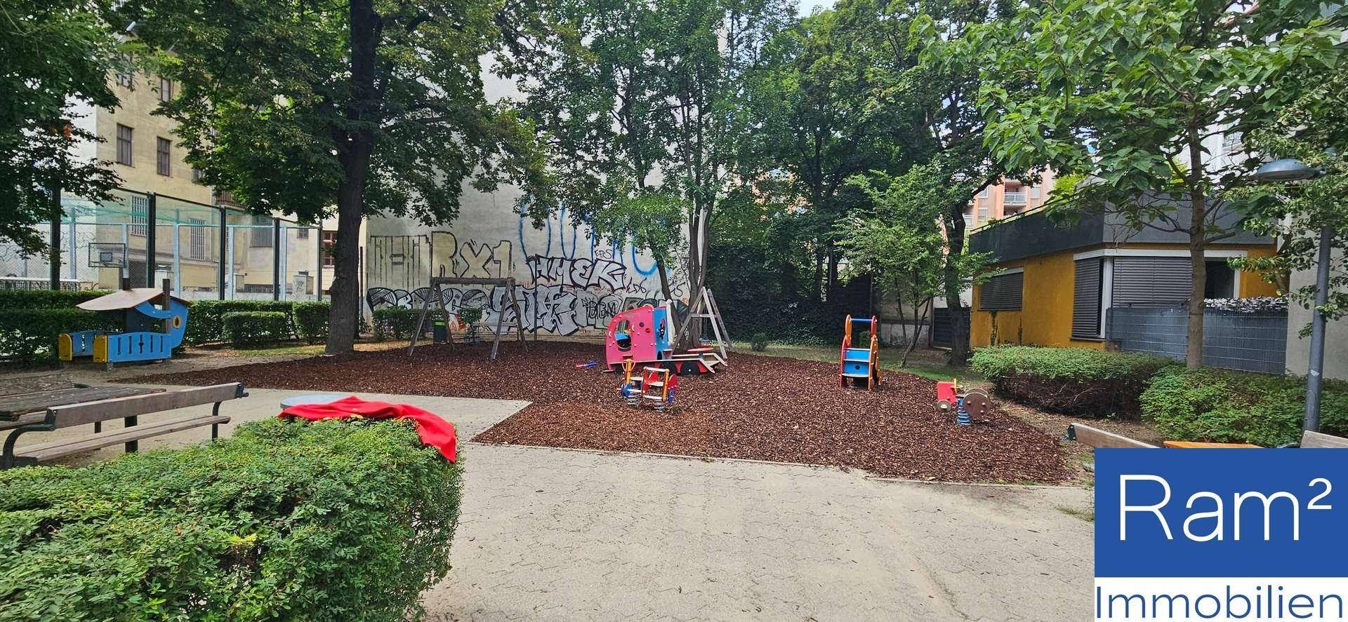 Bunter Spielplatz mit Holzschnitzeln und verschiedenen Spielgeräten unter Bäumen.