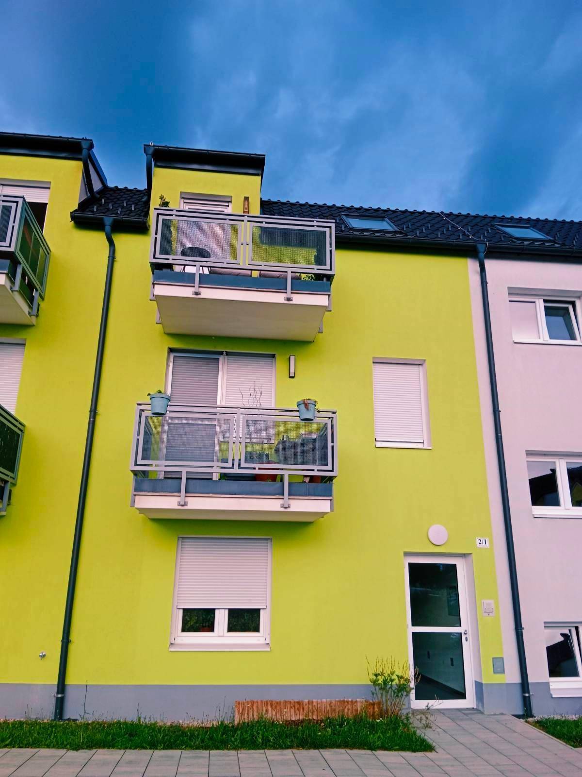 Mehrfamilienhaus mit leuchtend grüner Fassade und mehreren Balkonen.