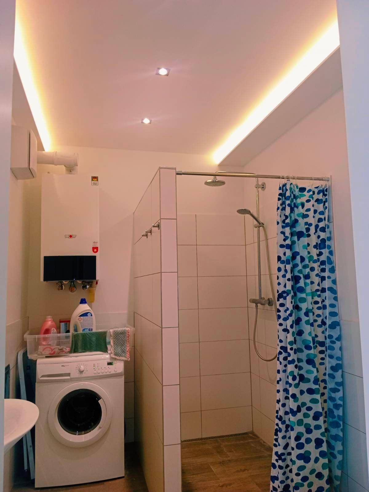 Modernes Badezimmer mit Dusche, Waschmaschine und indirekter Deckenbeleuchtung.