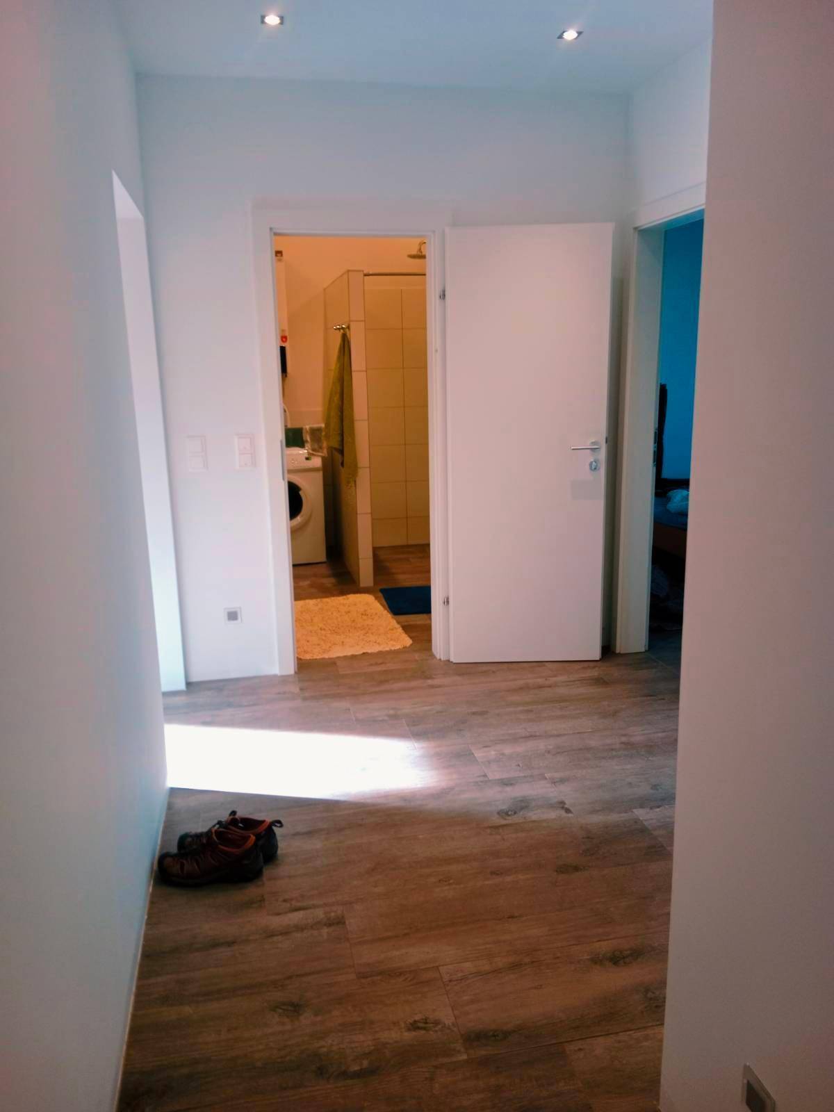 Heller Flur mit Holzboden, der den Blick in ein Badezimmer freigibt.
