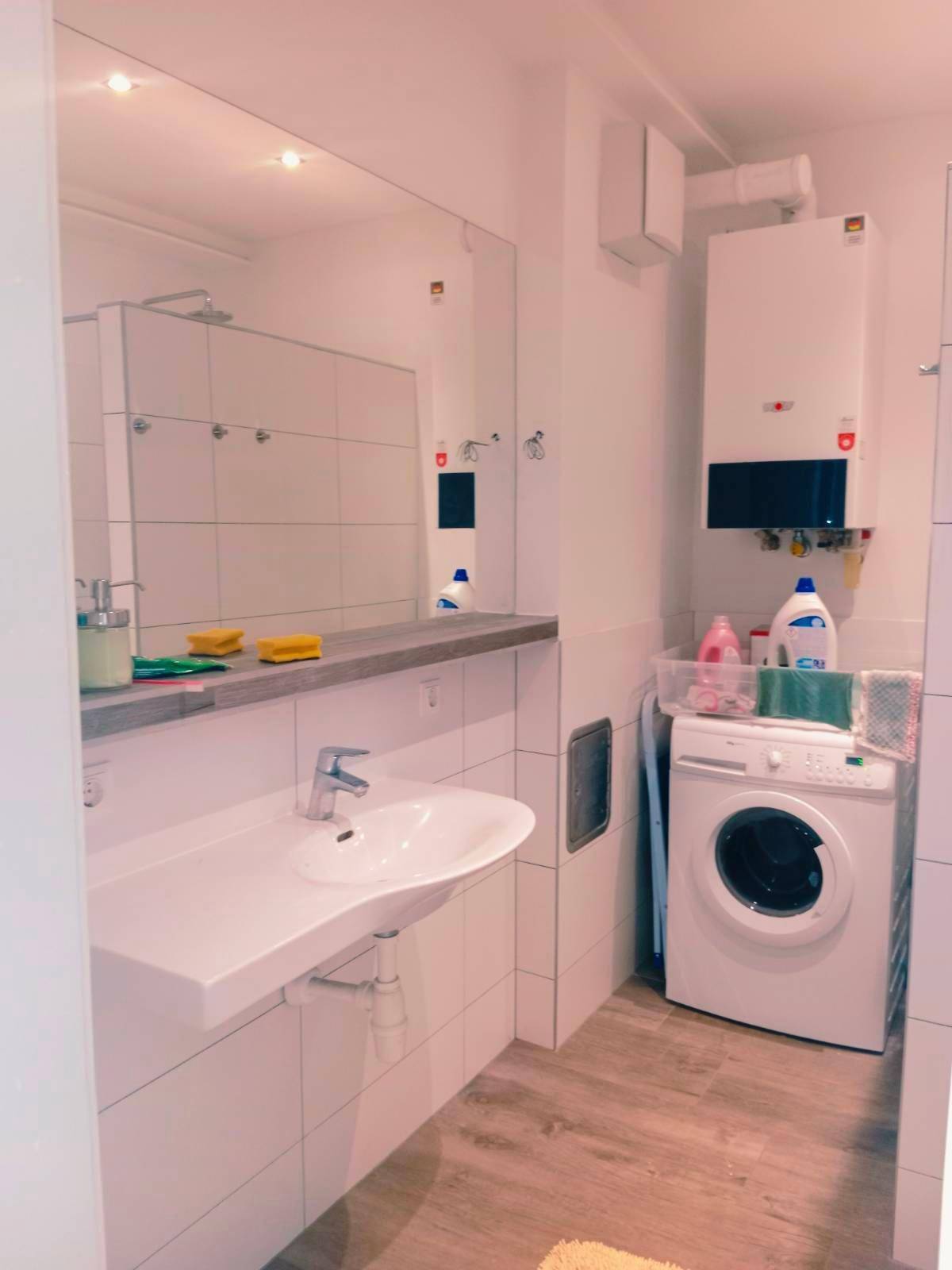 Badezimmer mit Waschbecken, großem Spiegel und integrierter Waschmaschine.