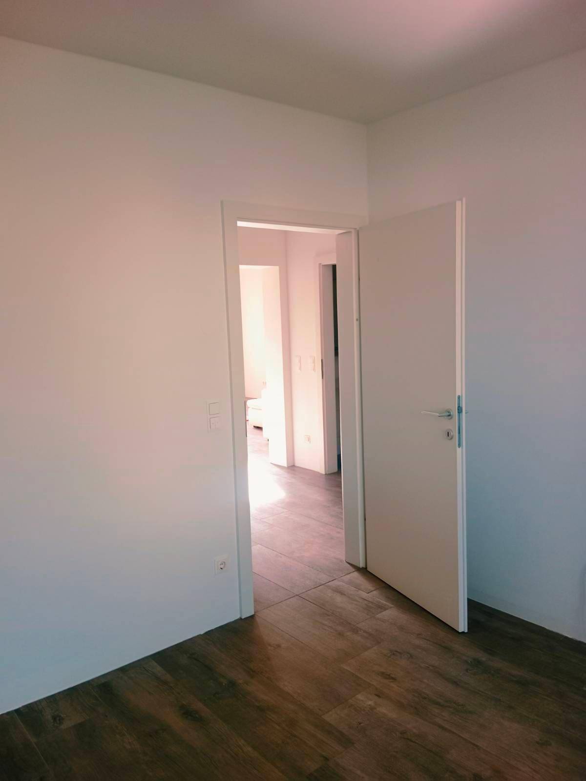 Heller Flur mit Holzboden und offener Tür zu weiteren Räumen der Wohnung.