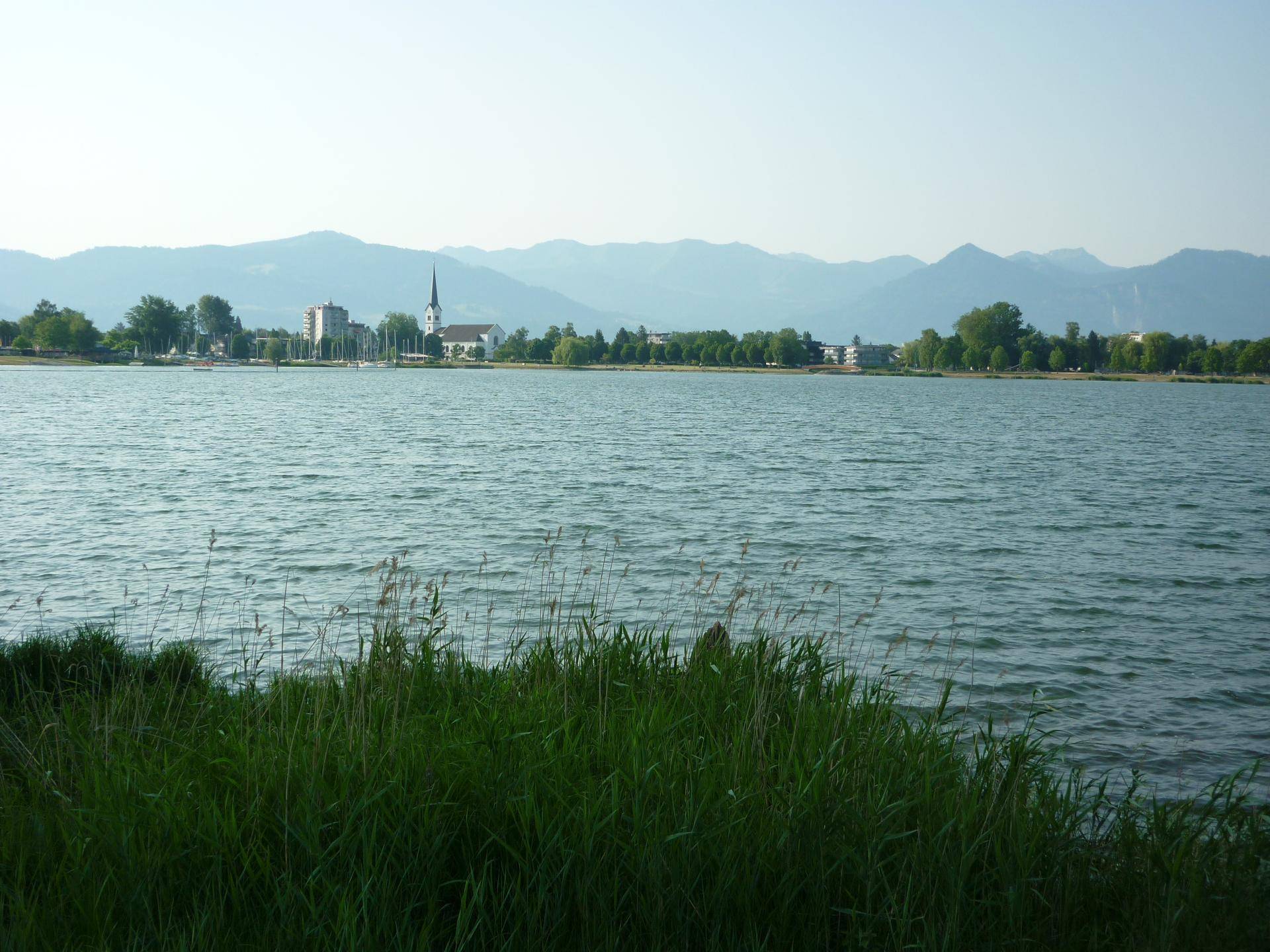Weitläufiger Seeblick mit einer Stadtkulisse und majestätischen Bergen im Hintergrund.