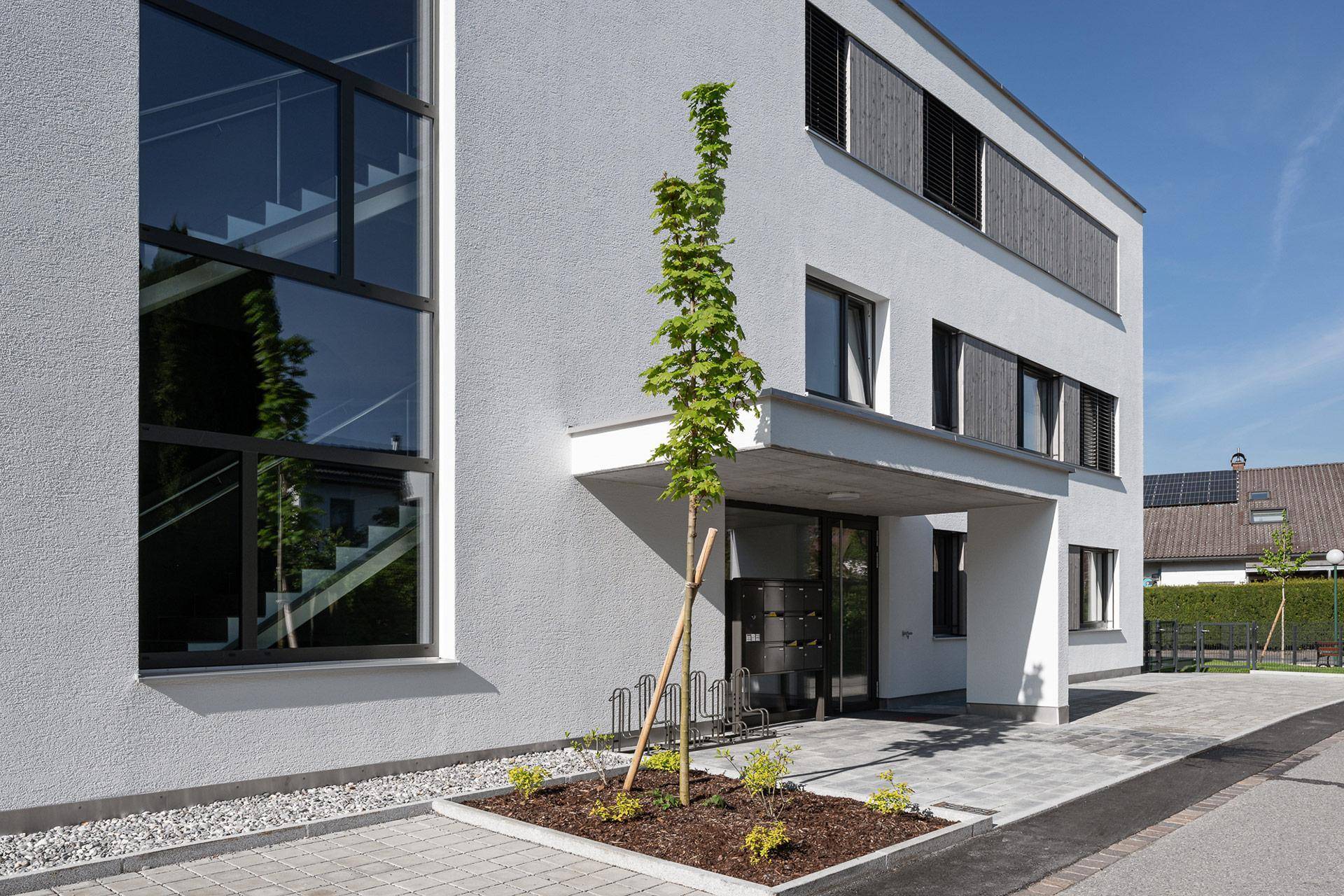 Eingangsbereich eines modernen Mehrfamilienhauses mit großen Glasflächen und Fahrradständern.