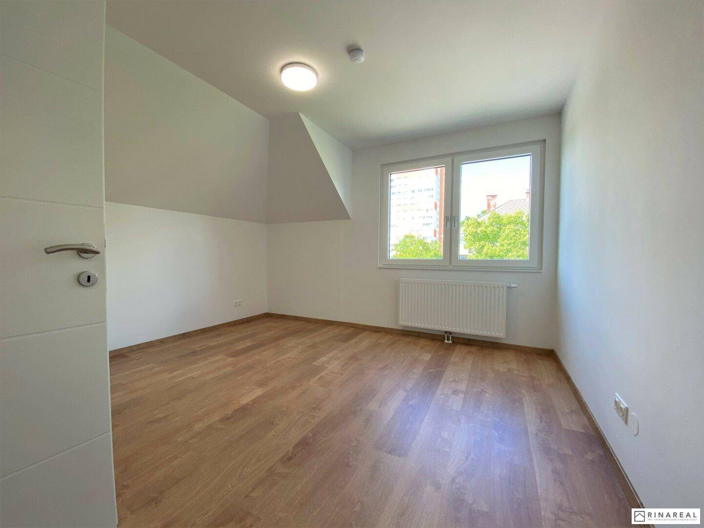 Helles Schlafzimmer mit Holzboden und Fenster, das einen Blick auf die Umgebung bietet.