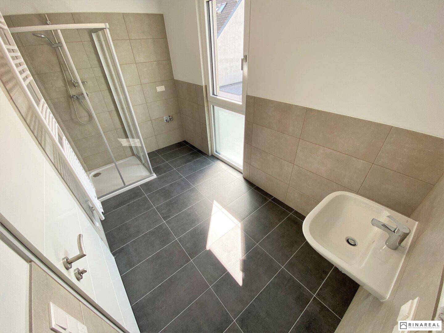 Modernes Badezimmer mit Dusche, Waschbecken und großformatigen Fliesen in neutralen Tönen.