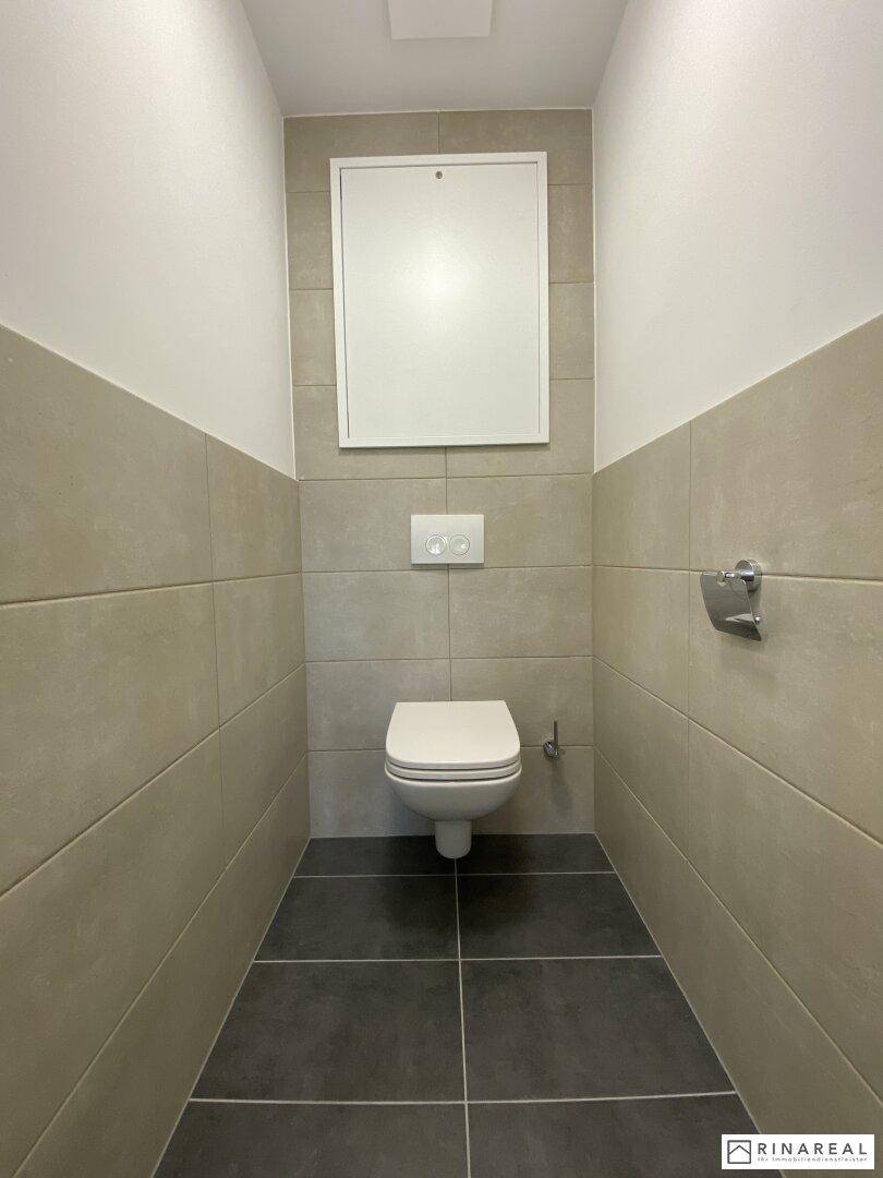 Separates Gäste-WC mit Wand-WC und modernen Fliesen in neutralen Farbtönen.